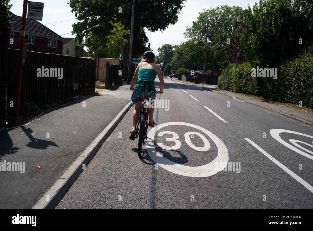 A healthy fit middle-aged women rides bike over a 30mph painted road sign dressed in summer clothing out on a leisure cycle ride. Stock Photo