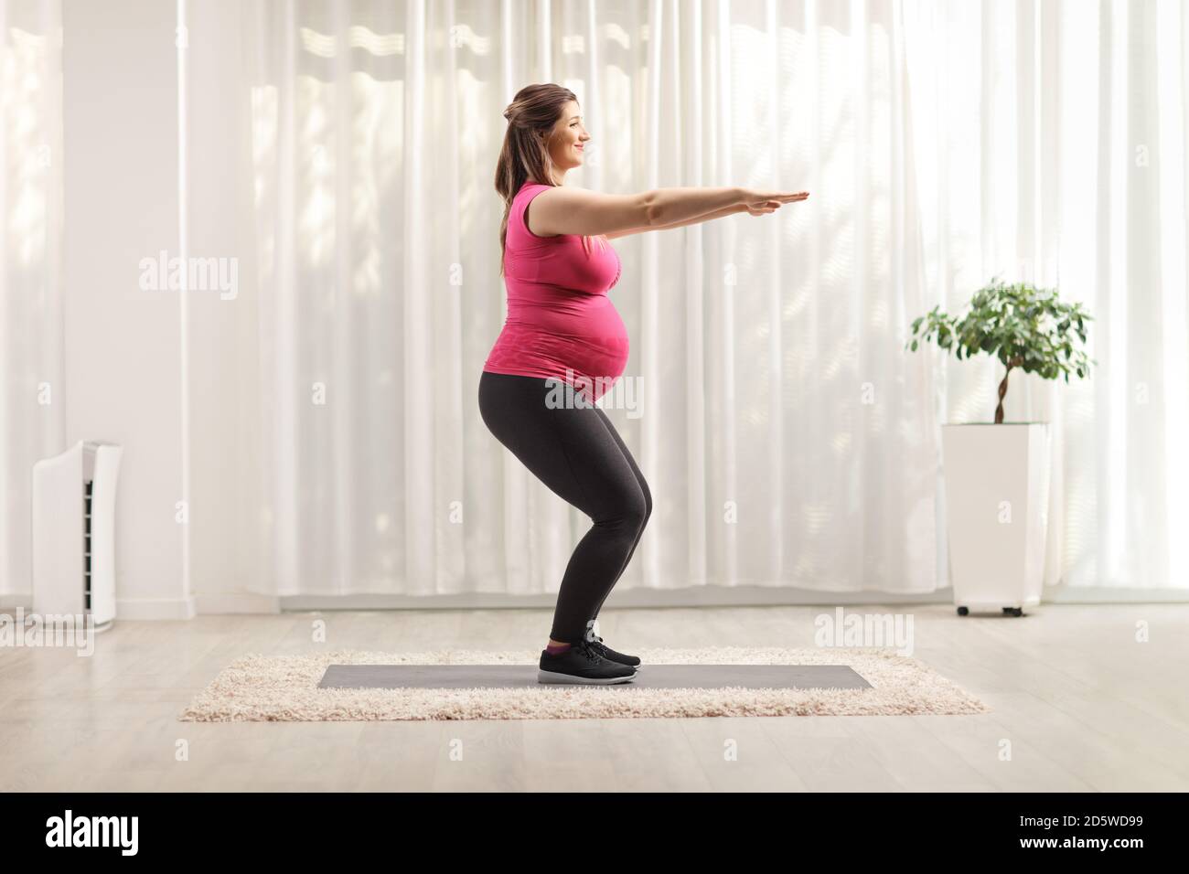Full length profile shot of a woman doing pregnancy exercises at home ...
