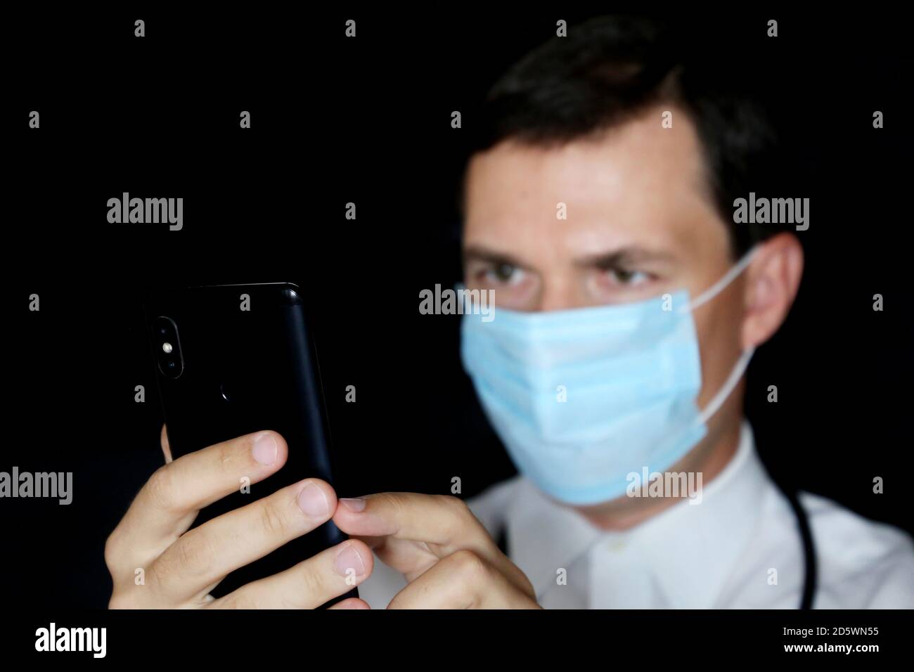 Doctor in mask using smartphone, mobile phone in male hand close up. Concept of appointment online, medical exam Stock Photo