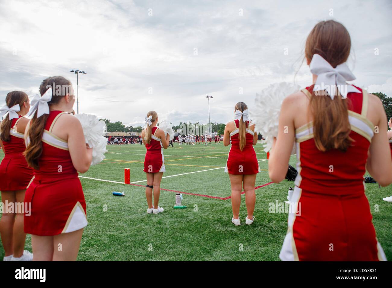 A group of cheerleaders with bows in hair stand on football field Stock Photo