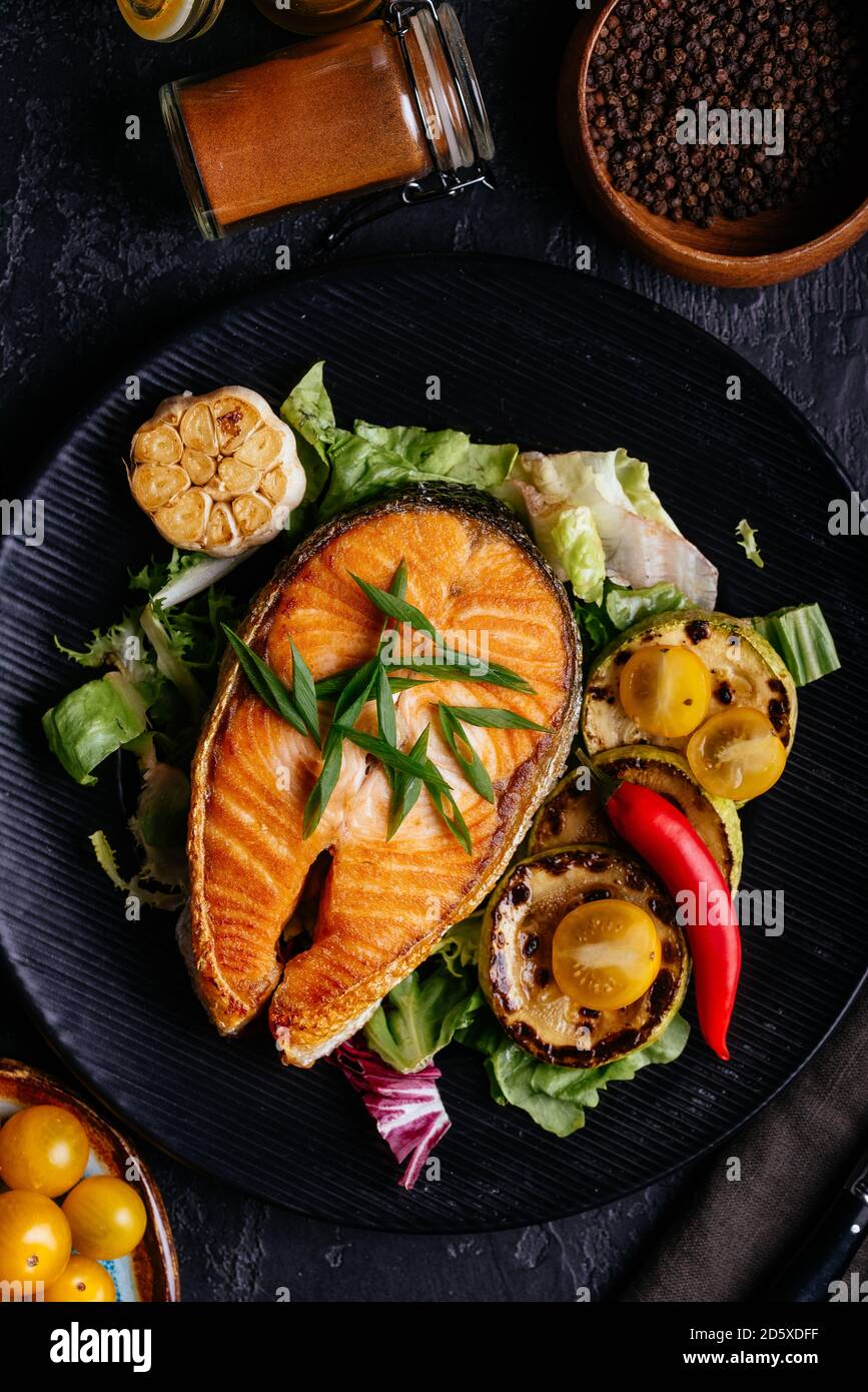 salmon steak baked on coals with vegetables on a black background Stock ...