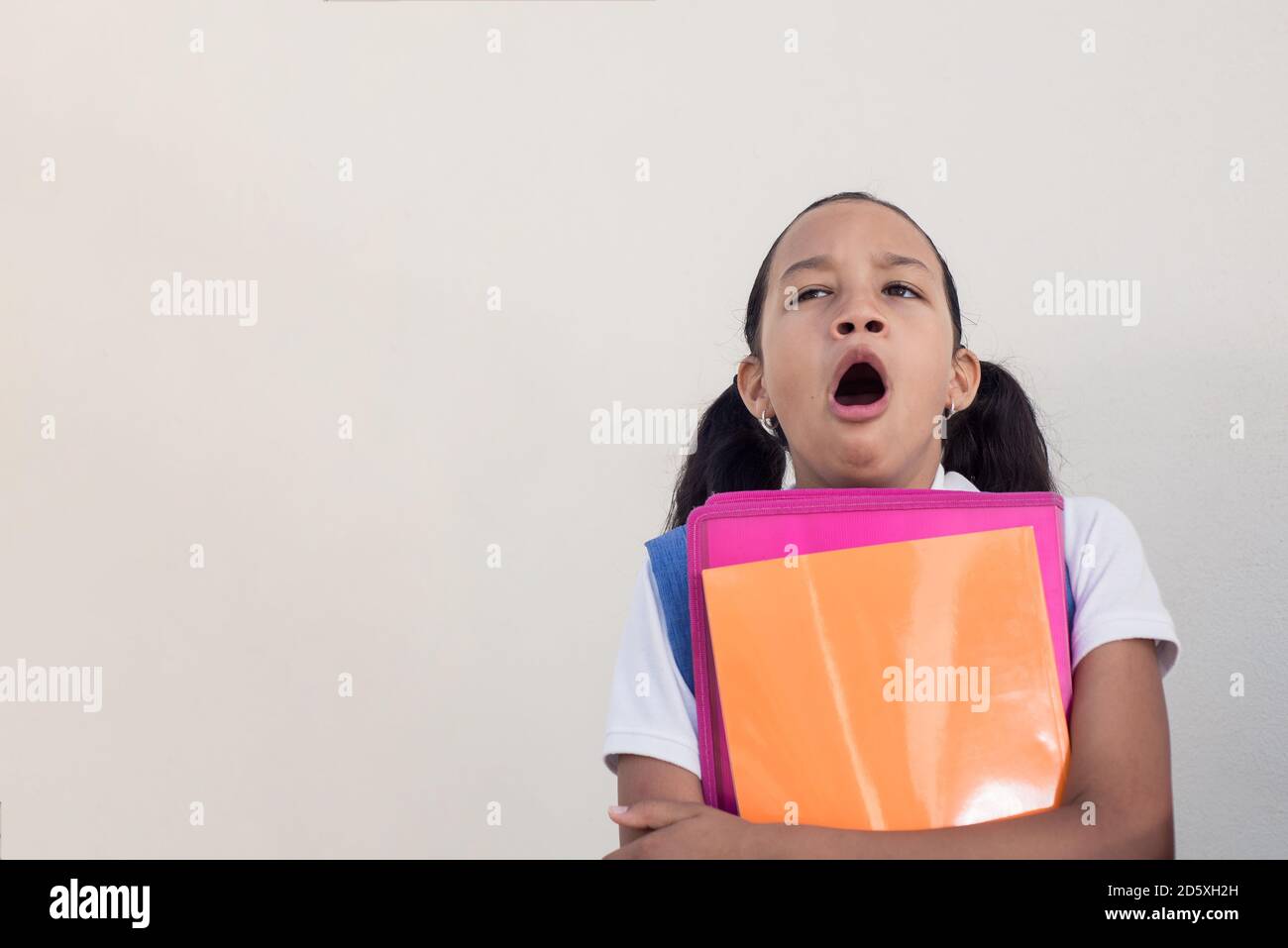 School girl yawning with notebooks and folders in hand. Boredom in school concept. Copy space for text. Stock Photo
