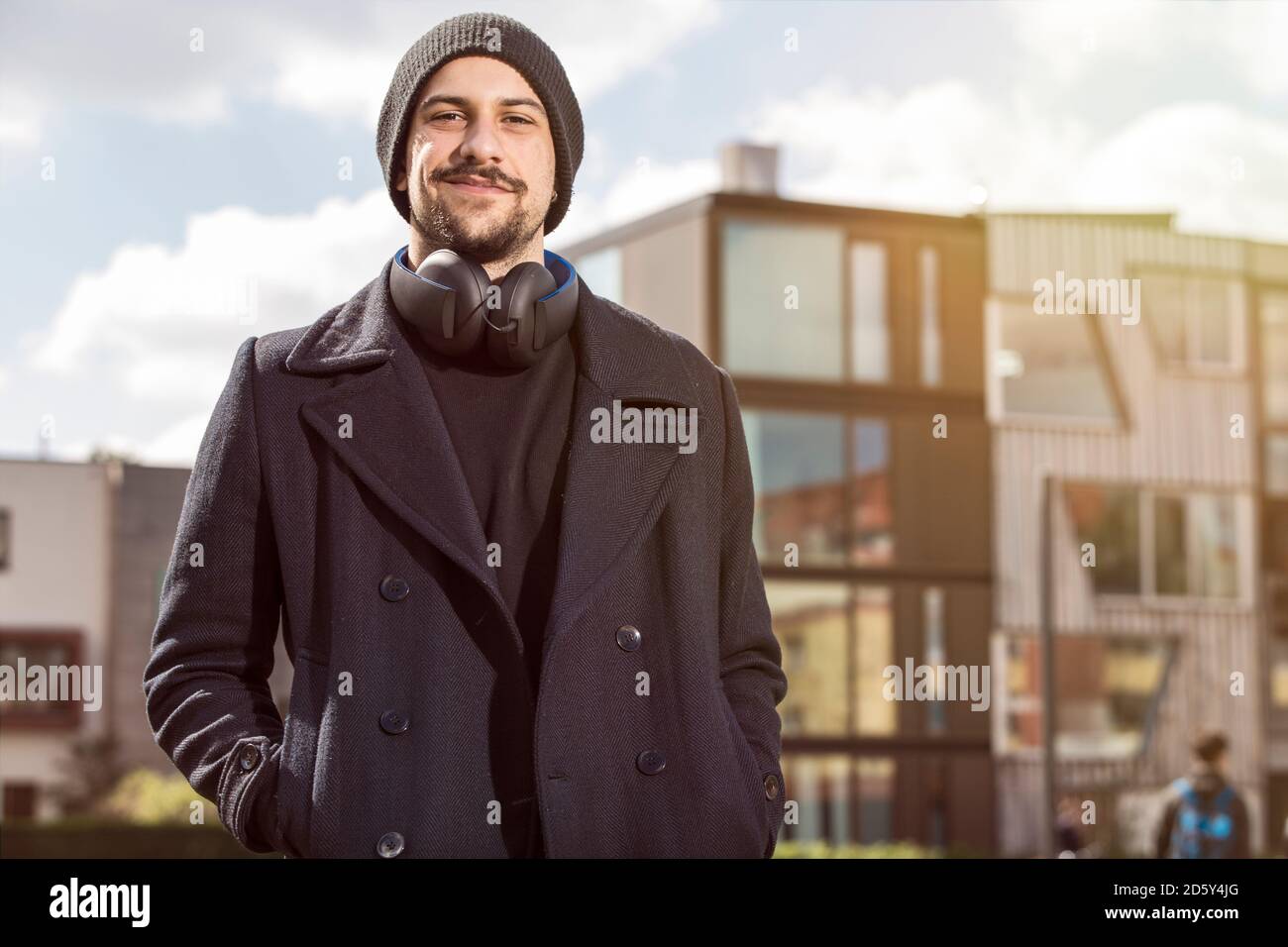Portrait of smiling young man with headphones wearing wool cap and black clothes Stock Photo