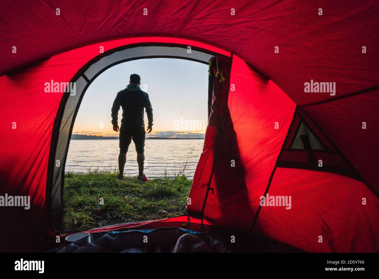 Man camping in Estonia, standing in front of tent, watching sunset Stock Photo