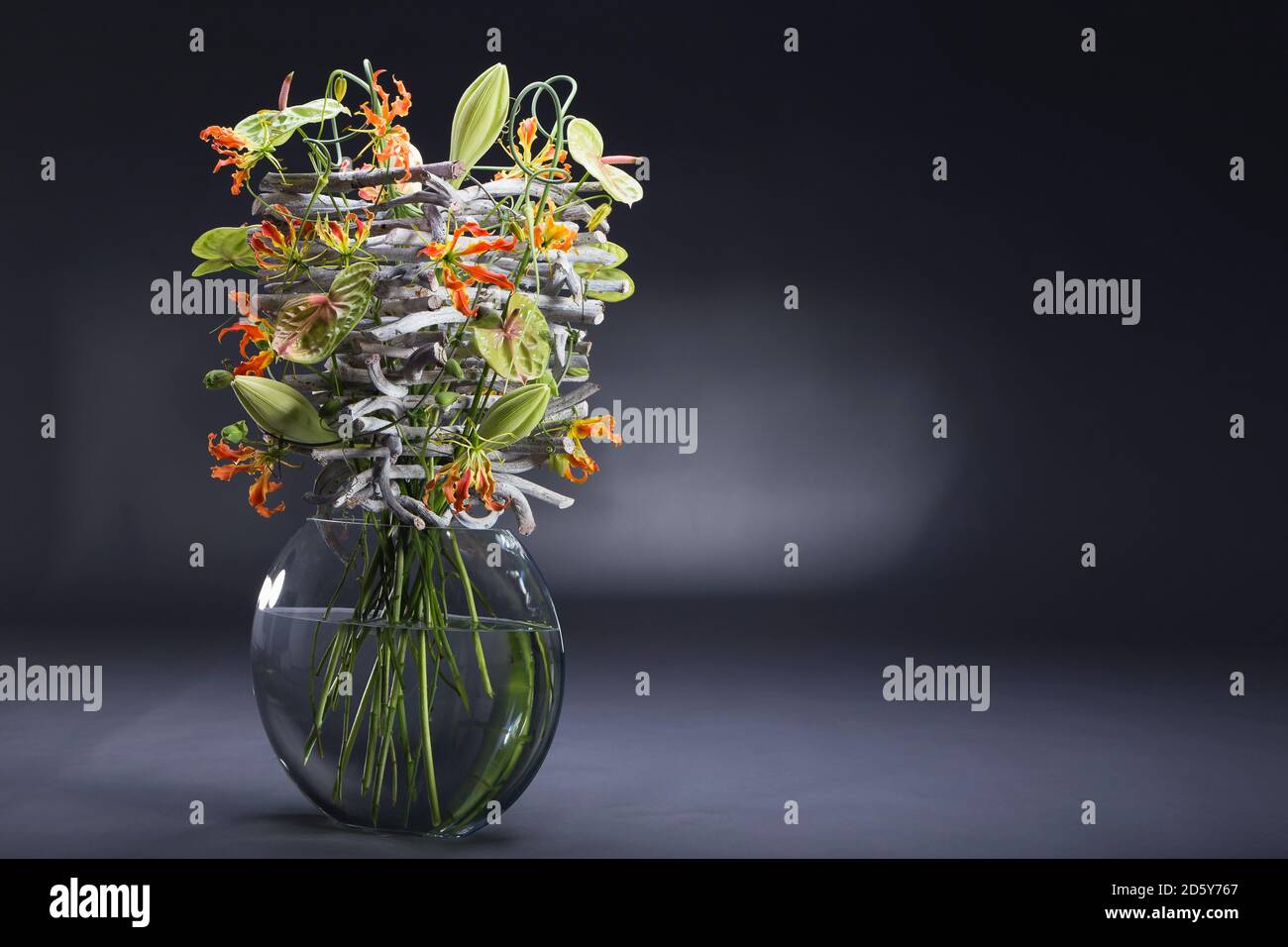 Floral arrangement of stone wood, Allium sativum, Anthurium, Gloriosa superba, Lilium longiflorum, Passiflora caerulea Stock Photo