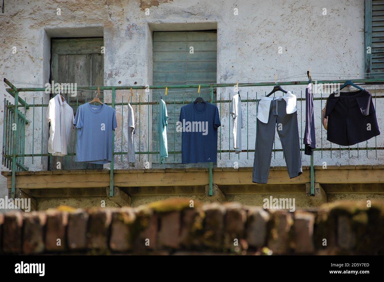 shades of blue clothes drying in the sun hanged on wire in foreground and old house facade in background in Italy Stock Photo