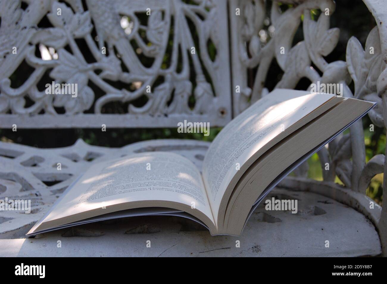 an open book on a white vintage cast iron bench in the home garden. Life at home. Relax Stock Photo