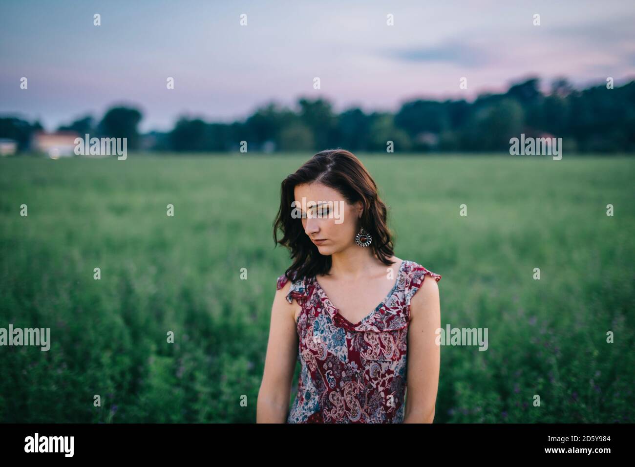 Portrait of a melancholic woman wearing a dress in a green field Stock Photo