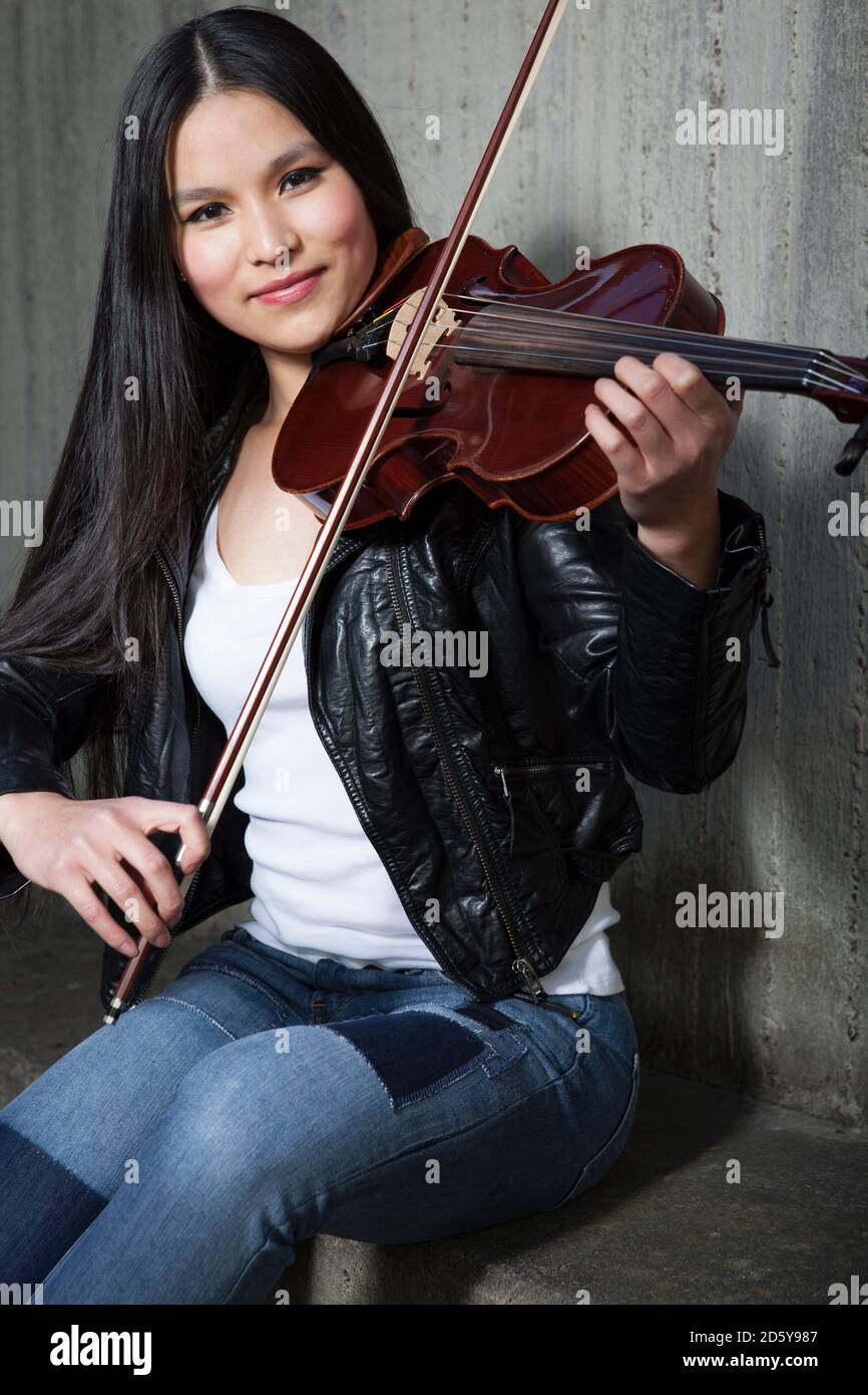 Portrait of young female Asian violinist in front of concrete wall