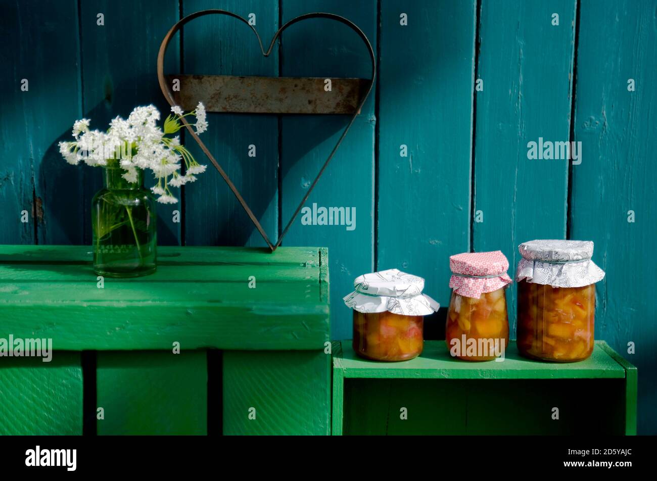 Three glasses of homemade rhubarb apricot jam, heart-shaped cutter and blossoming woodruff Stock Photo
