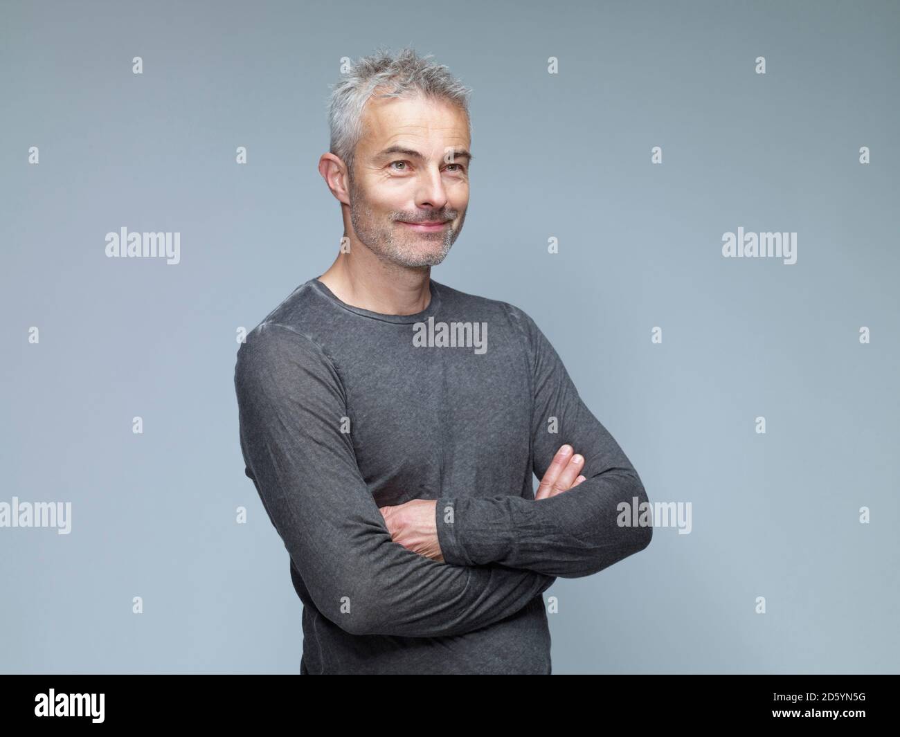 Portrait of smiling mature man with crossed arms in front of green ...