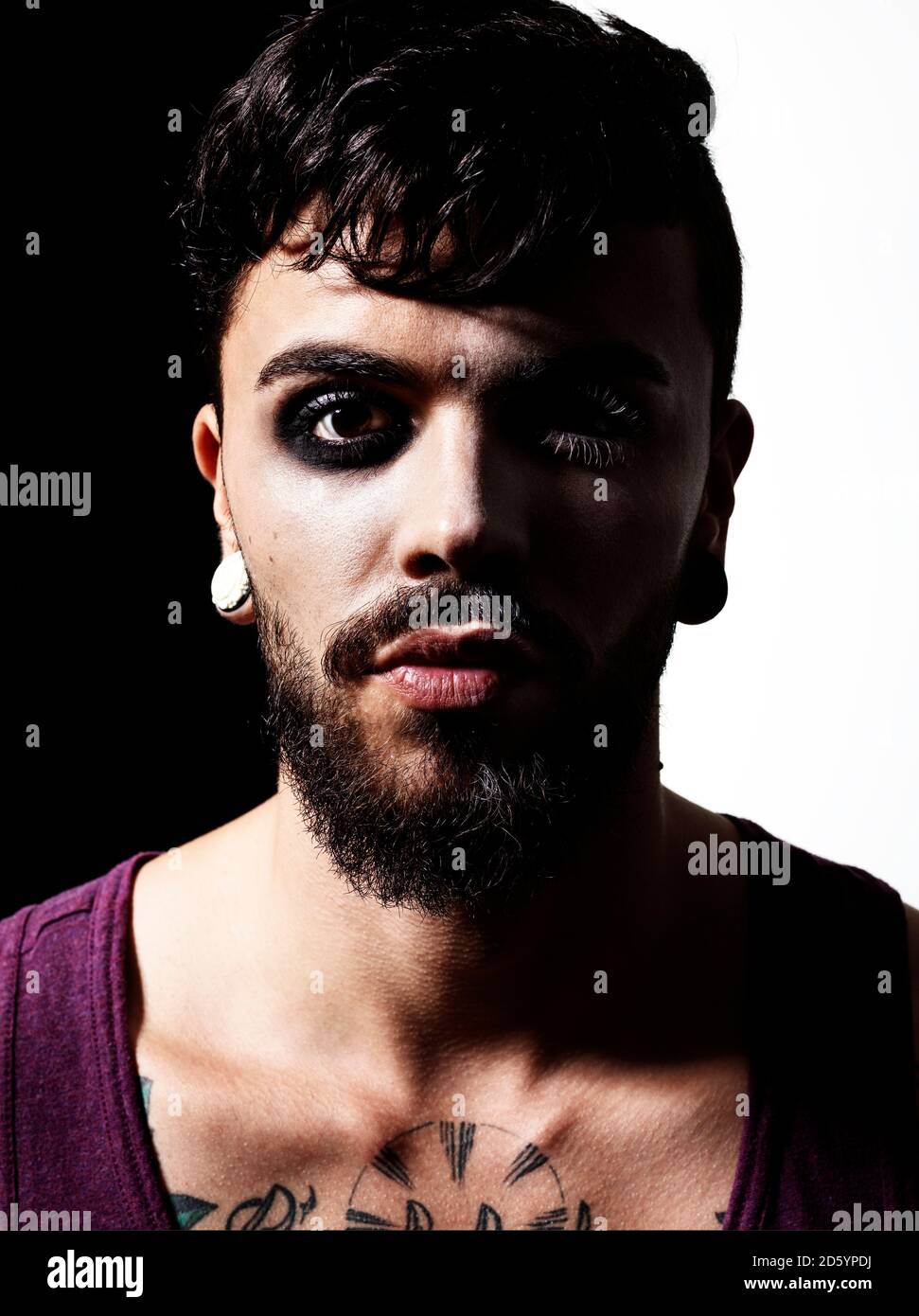 Portrait of man with full beard and earing wearing eye make up Stock Photo