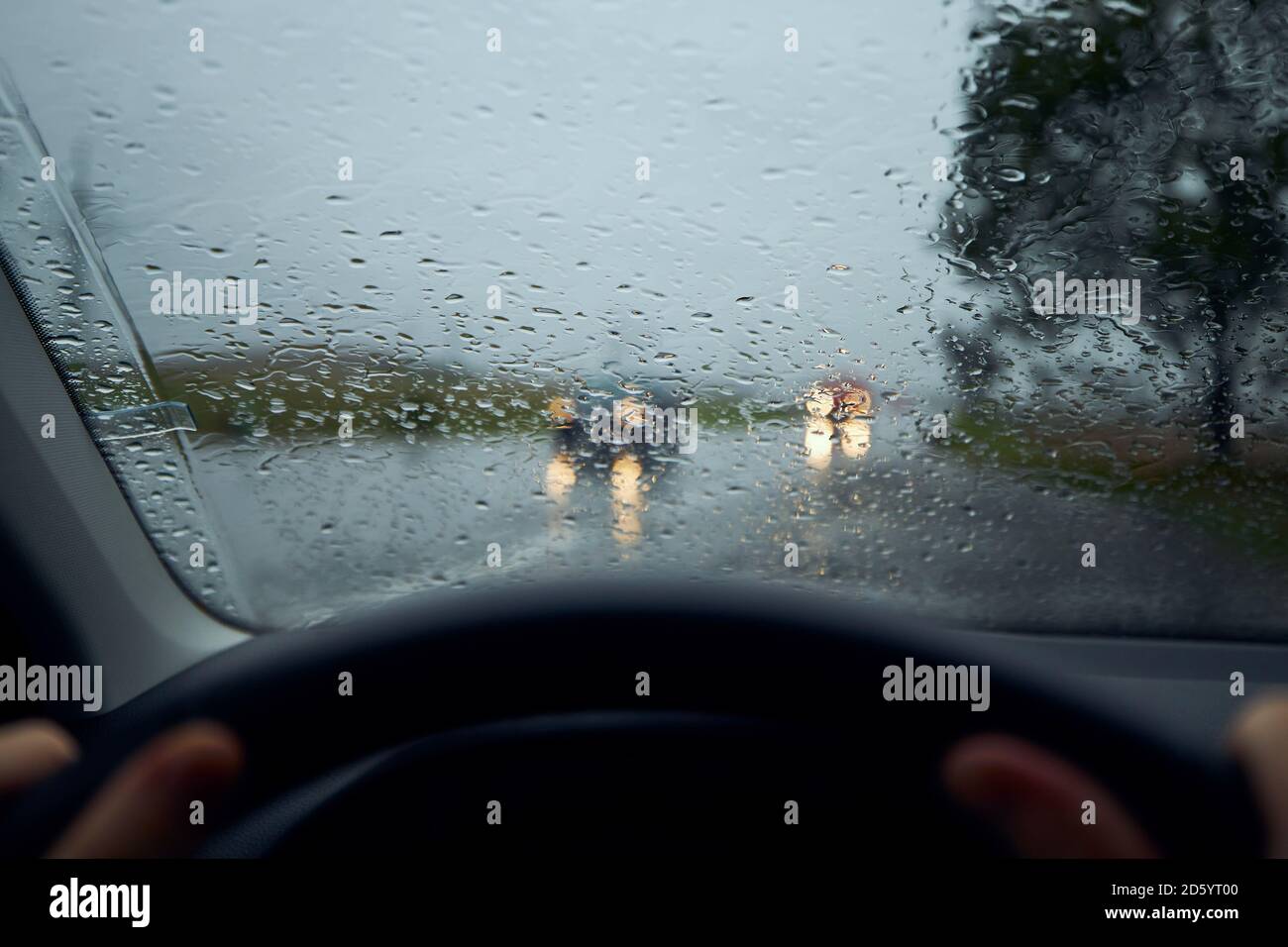 Driving in heavy rain. Raindrops on windshield of car against traffic in crossroad. Stock Photo