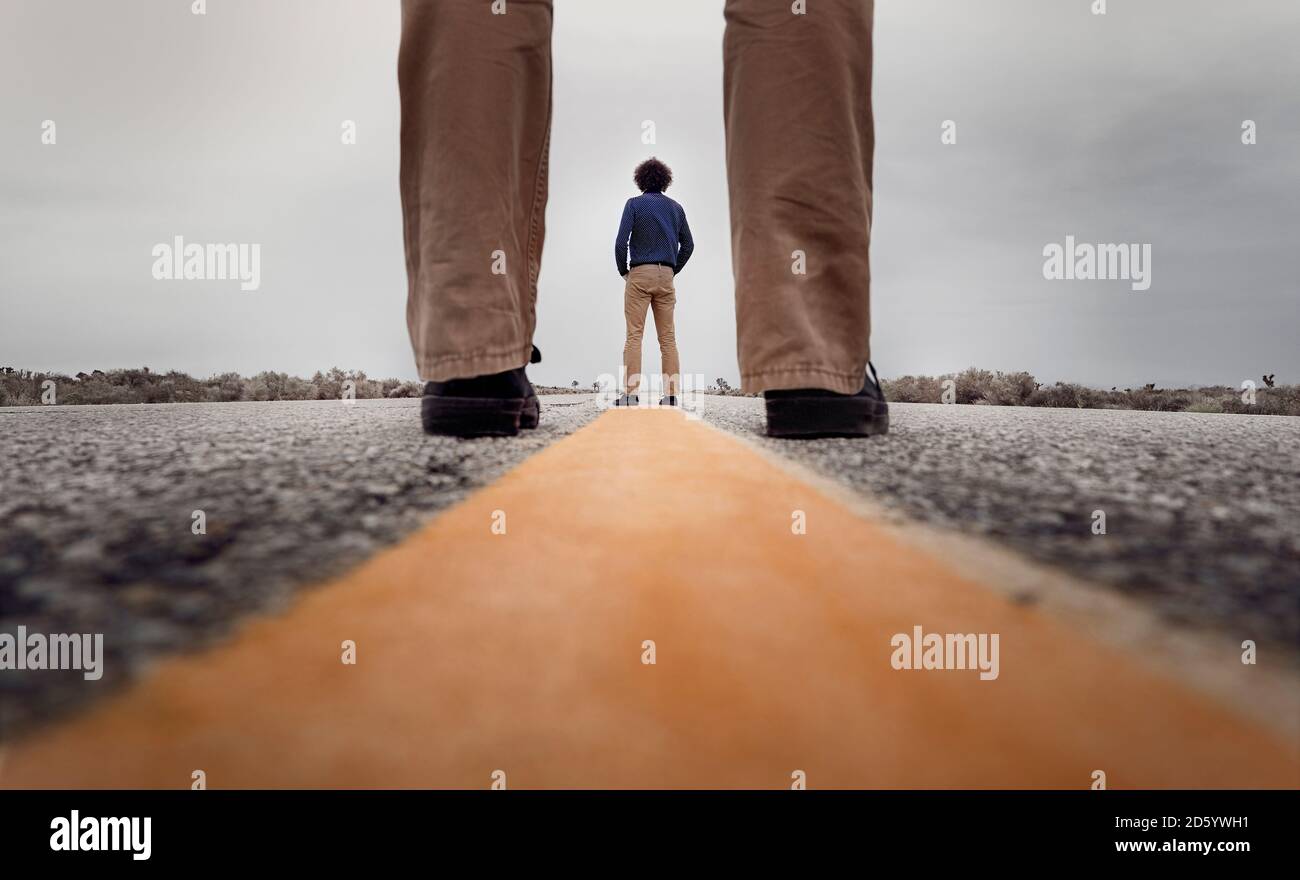 View through standing legs to a curly man standing on the medial strip of a road Stock Photo