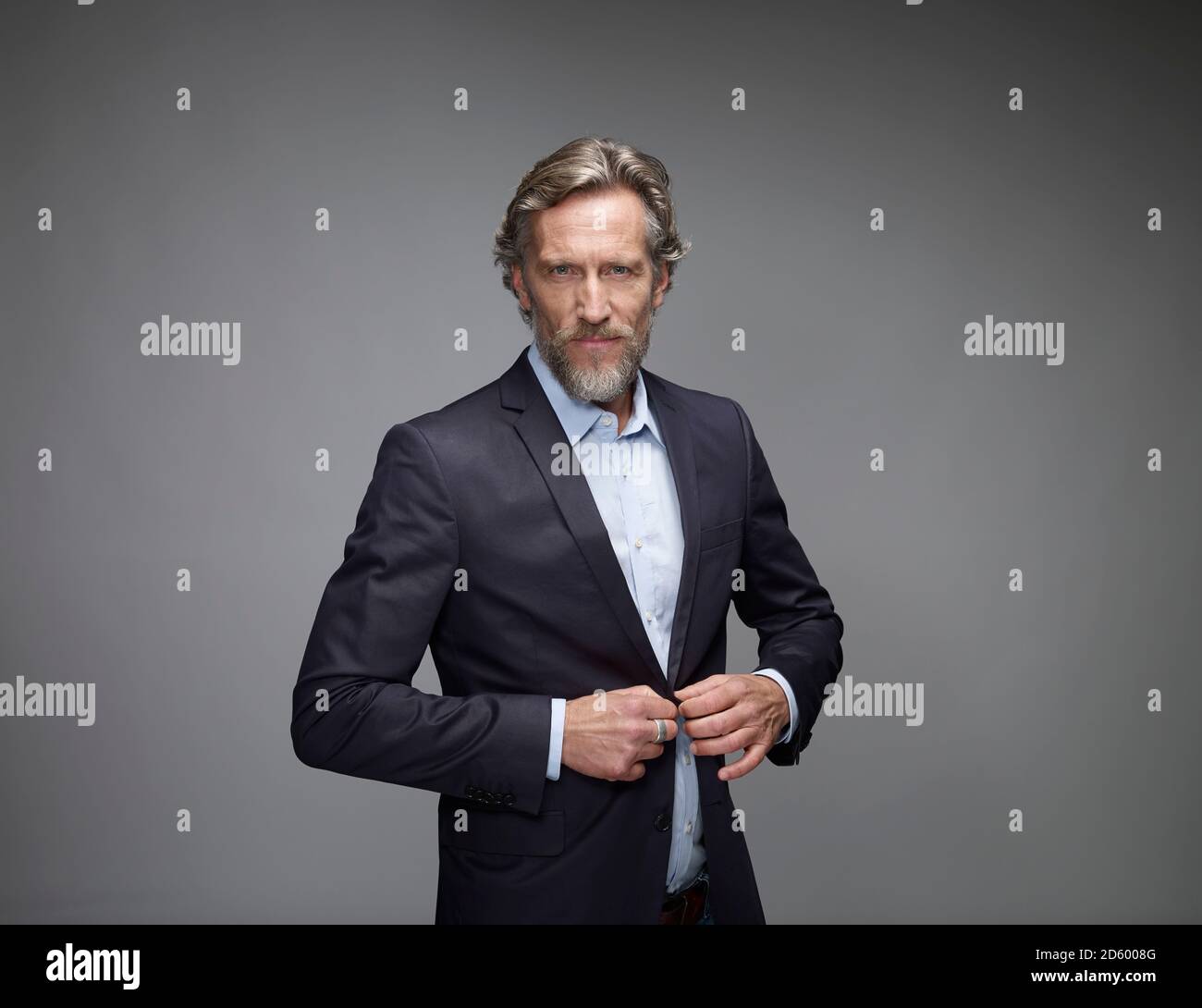 Portrait of mature man buttoning his jacket in front of grey background Stock Photo