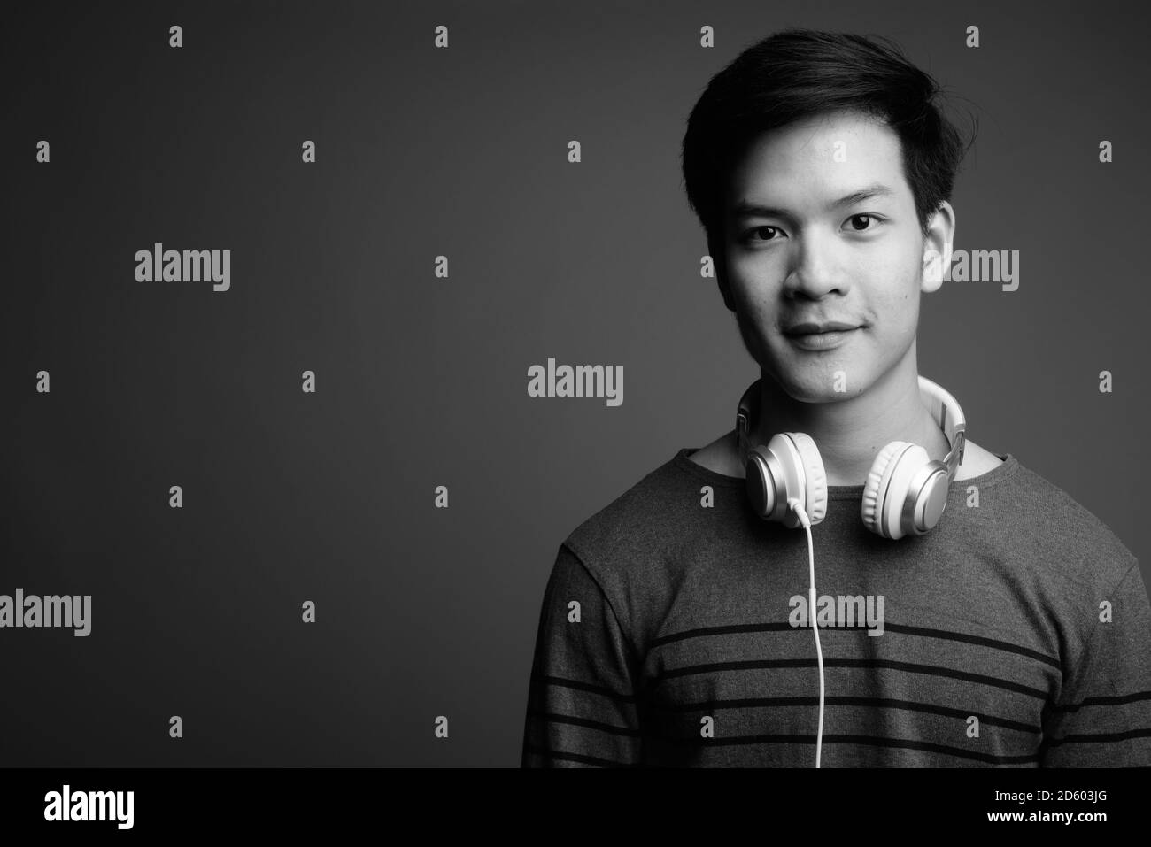 Young handsome Asian man wearing headphones against gray background Stock Photo