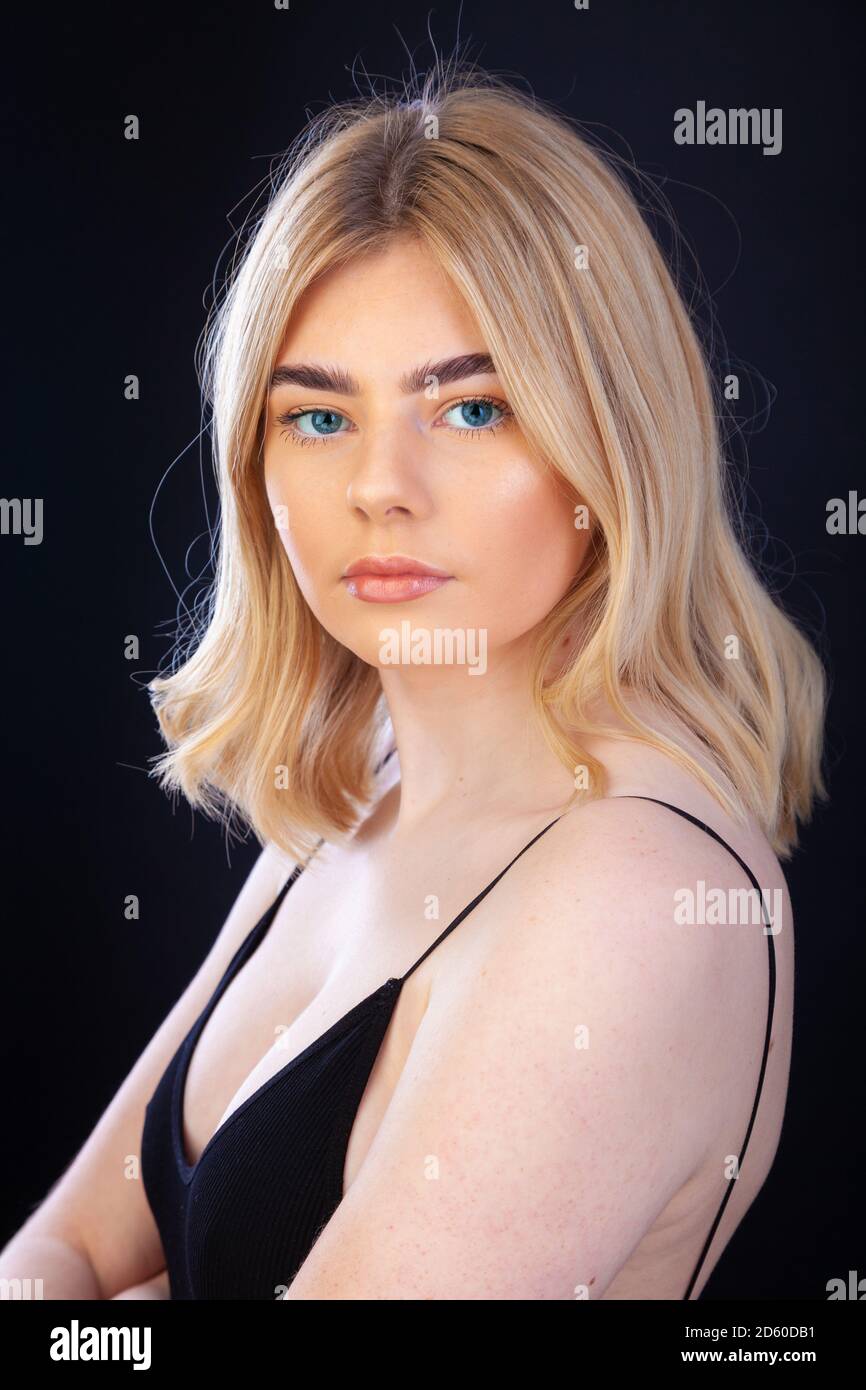 A beautiful young blond woman in her early twenties wearing a black skinny strap top and looking straight at camera. Stock Photo