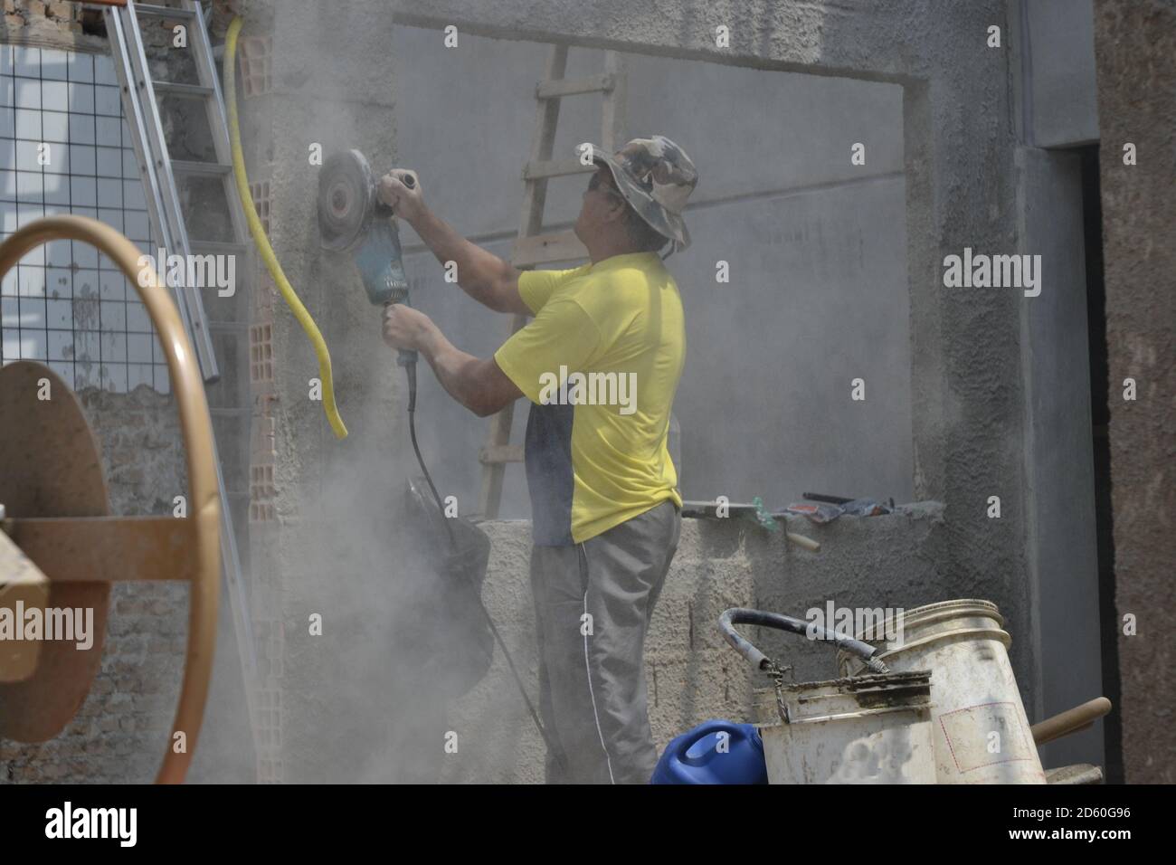 Worker or bricklayer, cutting wall with machine by hand, without protection, with buckets, aluminum ladder and ceramic tiles in the background Stock Photo