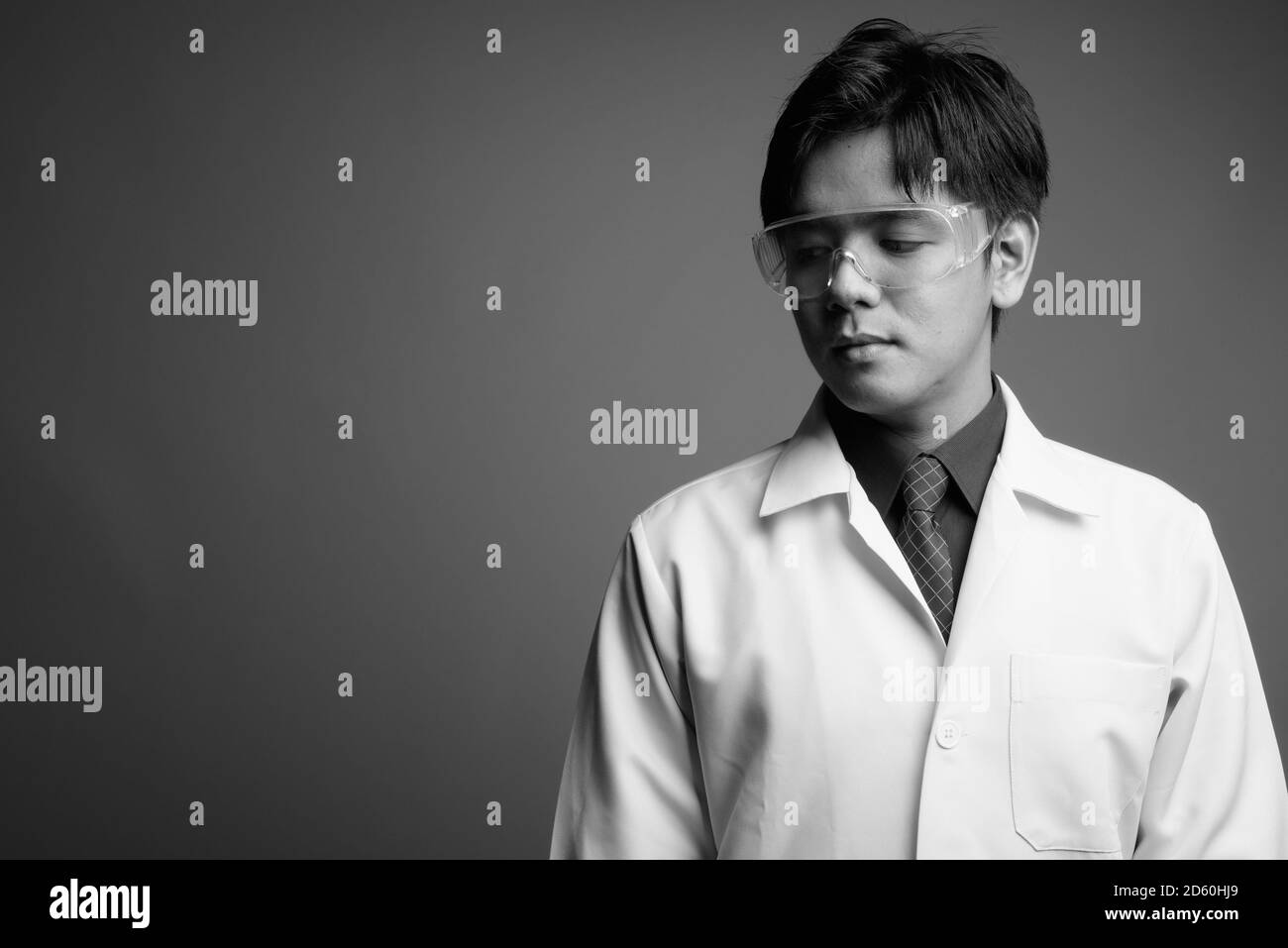 Young handsome Asian man doctor wearing protective glasses against gray background Stock Photo
