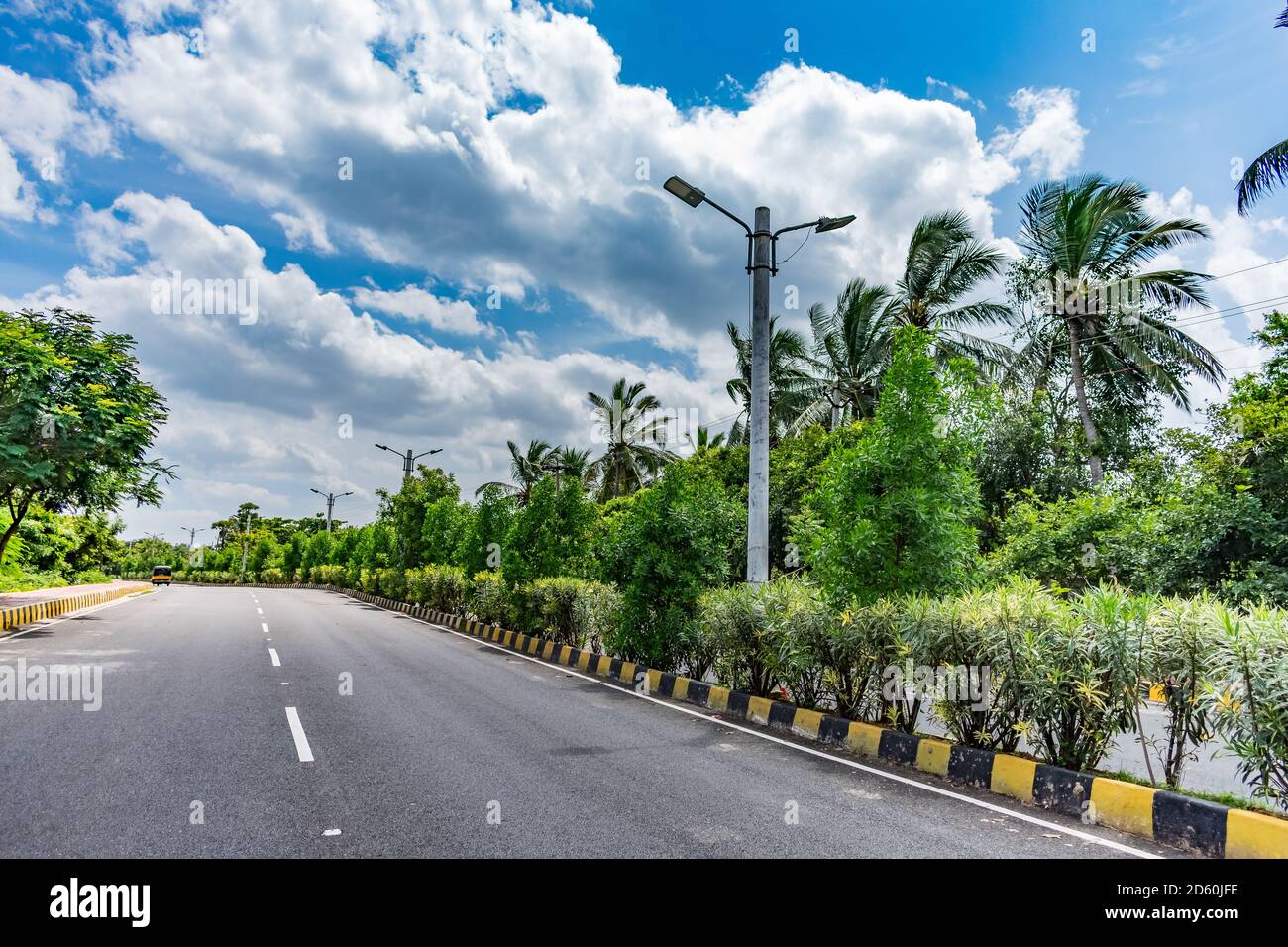straight road of national highway with trees plantation on center of road  with blue sky background Stock Photo - Alamy