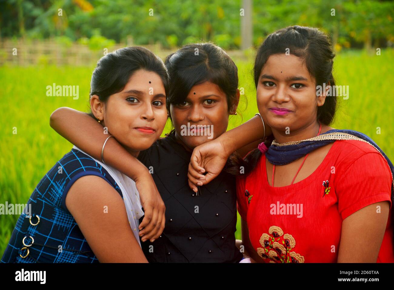 Close up of three teenage girls wearing colorful traditional Indian dresses smiling in a paddy field of West  Bengal, selective focusing Stock Photo