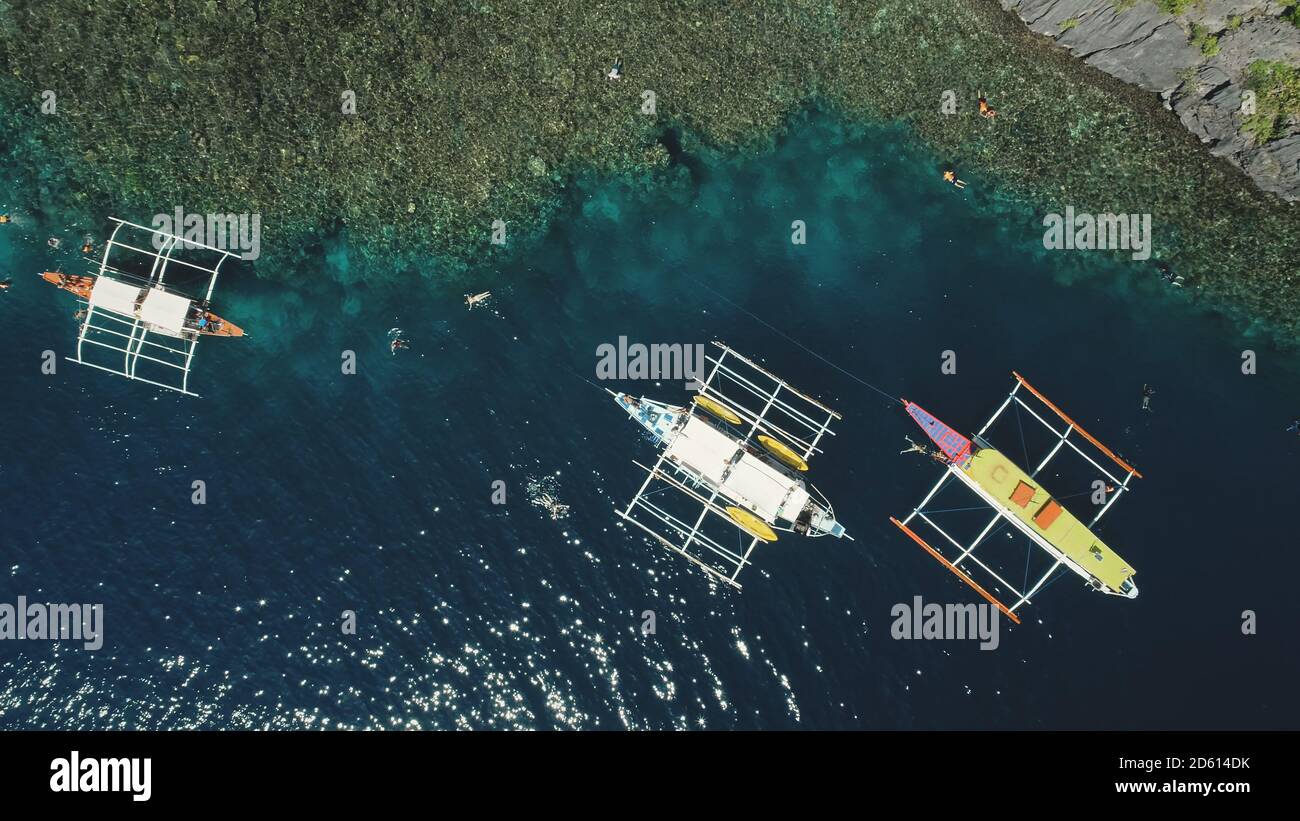 Top down of boats at green mount ocean coast aerial view. Epic summer landscape with vessels at rock shore. Nature beauty of tropic mountain isle Palawan, El Nido Islands, Philippines, Asia. Stock Photo