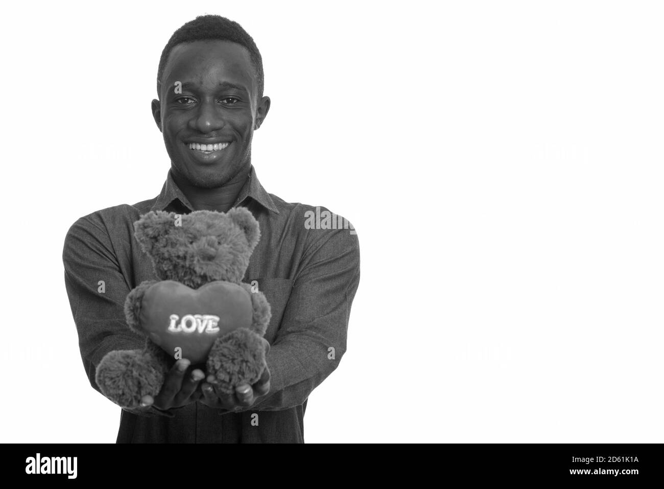Young happy African man smiling and giving teddy bear with heart and love sign Stock Photo