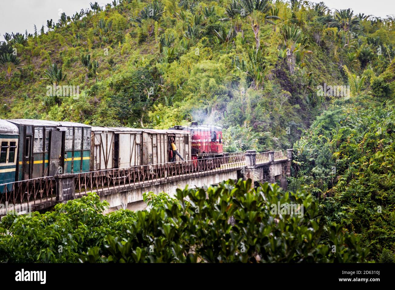 An Old train in Madagascar going through the jungle from Fianarantsoa to Manakara, A man gets to touch the bridge with his leg while train is running. Stock Photo