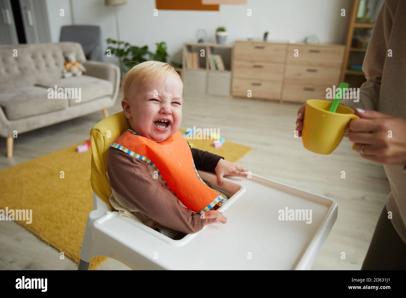Cute baby boy wearing bib sitting baby chair while his mother feeding ...