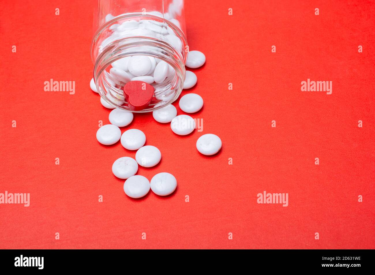 White medical pills spilling out of pills bottle, red background