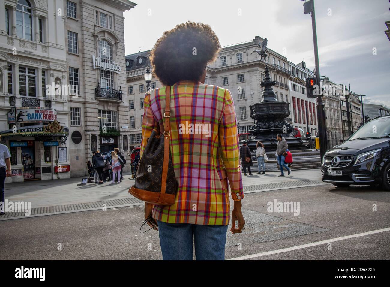 Lady wearing a colourful jacket with an afro hairstyle crossing the road onto Piccadilly Circus in London, England, United Kingdom Stock Photo