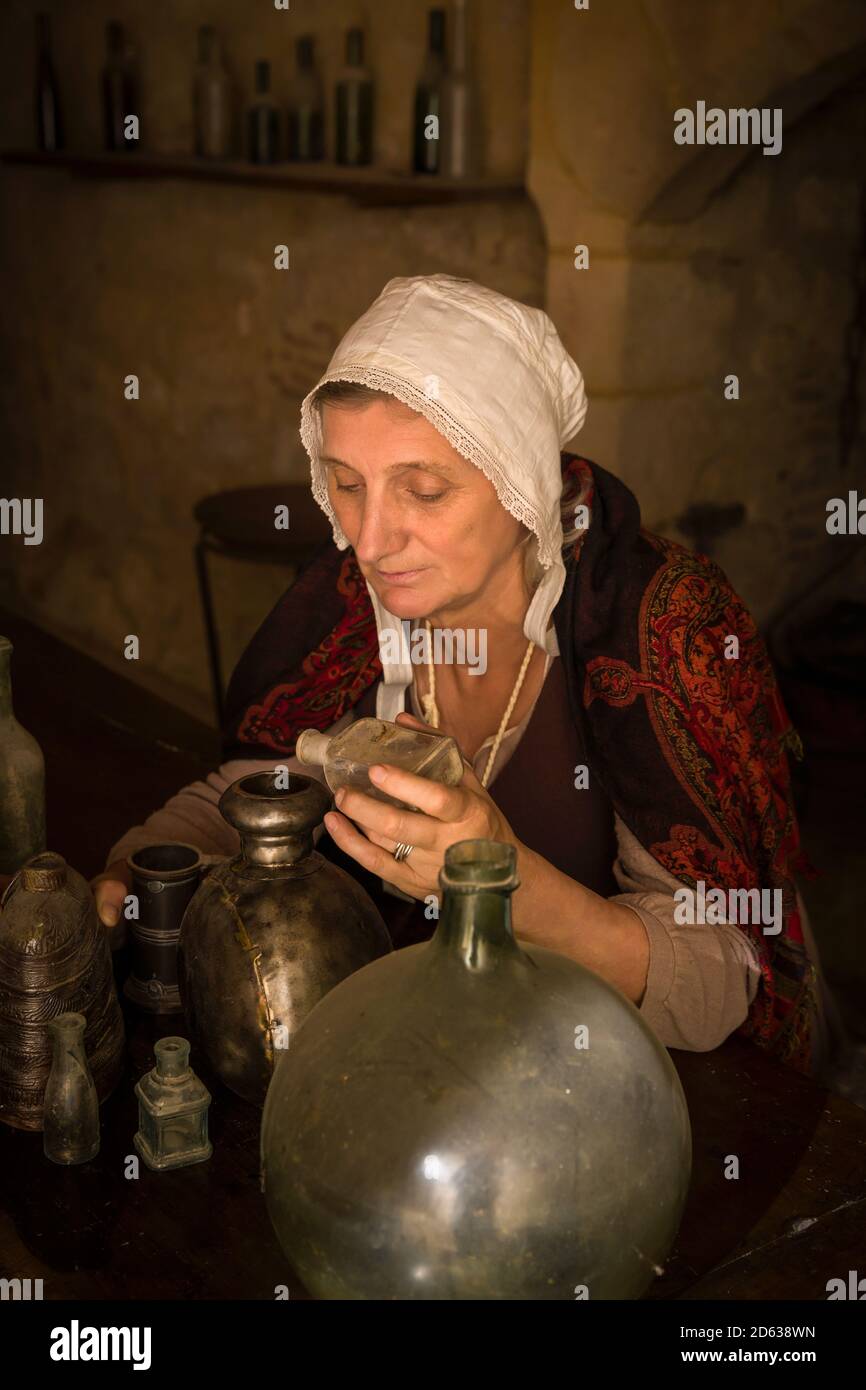 Woman in medieval outfit working as an alchemist or witch in the kitchen of a French medieval castle - with property release Stock Photo