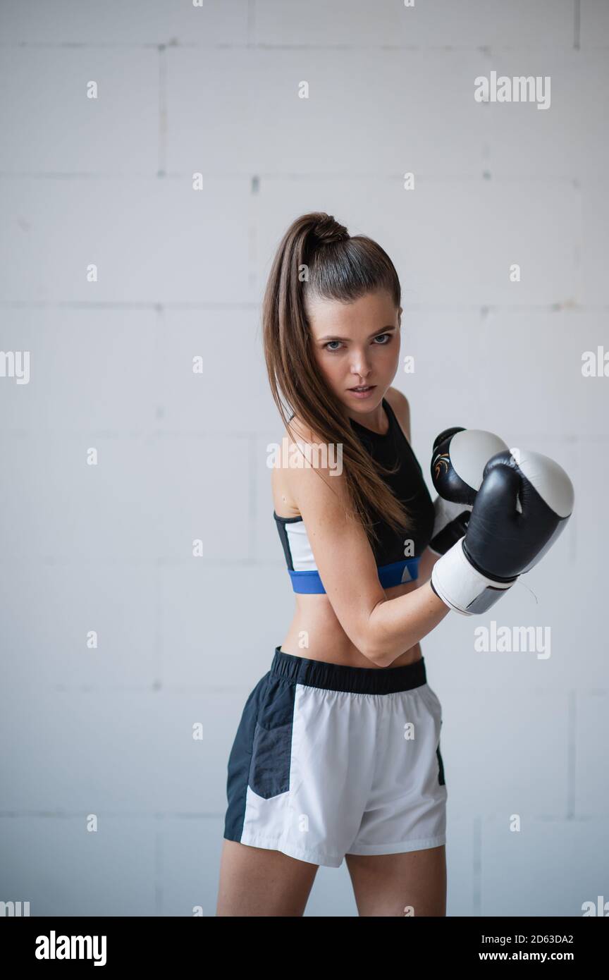A pretty female athlete in boxing gloves and sports uniform stands against  a white brick wall Stock Photo - Alamy