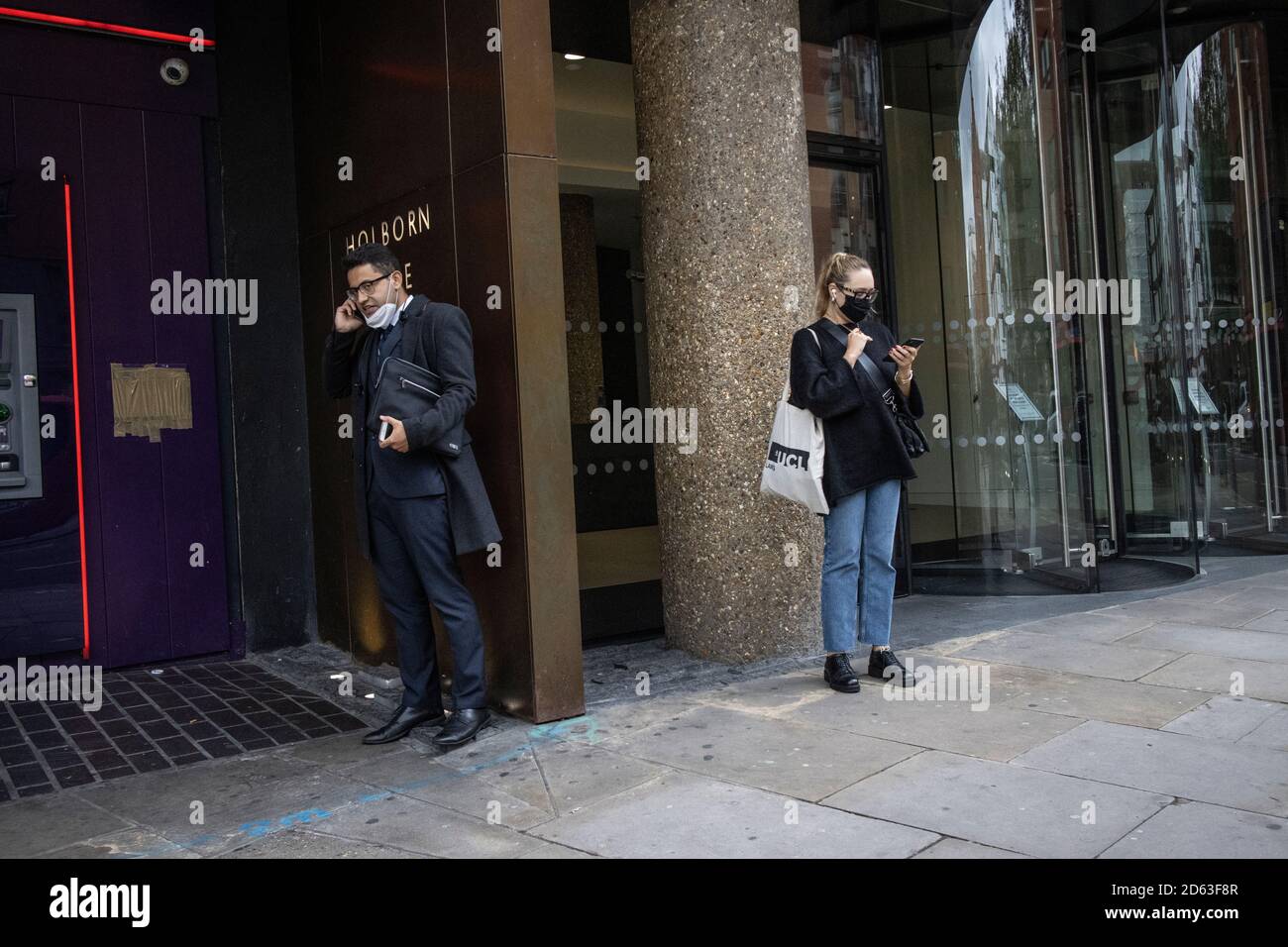 Business man on his phone wearing his facemask around his chin whilst stood at Holborn Gate, High Holborn, central London, Stock Photo