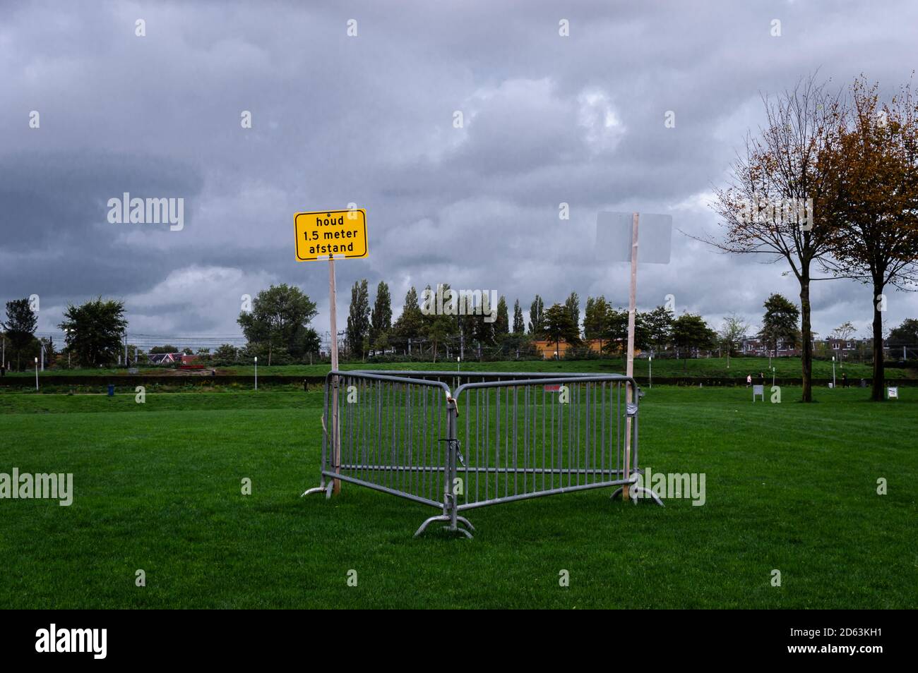 Translation: Keep 1.5 distance.  A yellow warning sign in the middle of a grass field of Amsterdams Wester Park. Hardly no one is outside Stock Photo