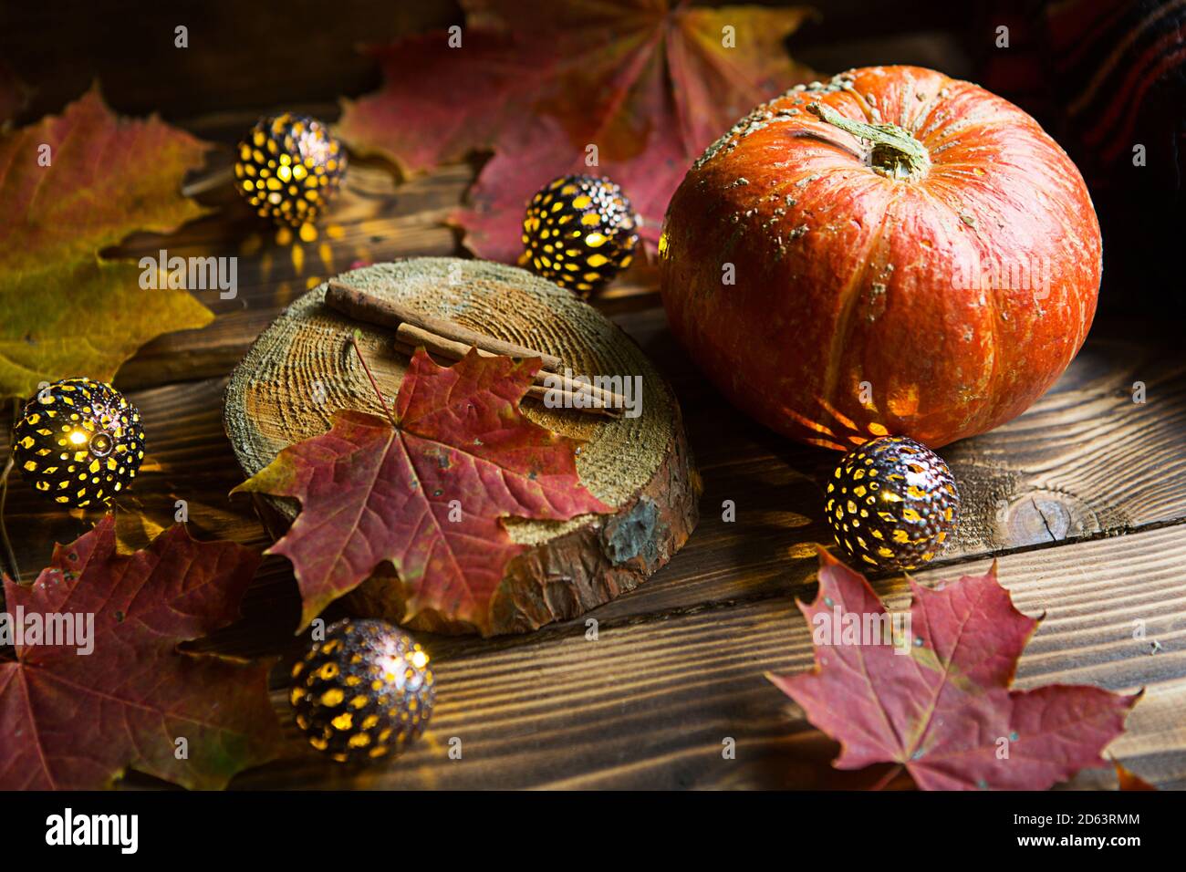 Orange natural round pumpkin on a wooden table with fallen yellow and red maple leaves, cinnamon sticks. Lights garlands, warm autumn atmosphere, than Stock Photo