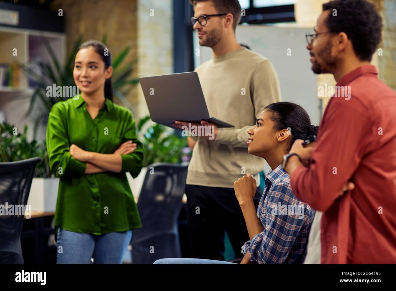 Group of young diverse multi ethnic business people using laptop and discussing project results while standing together in modern office. Business, teamwork, cooperation concept Stock Photo