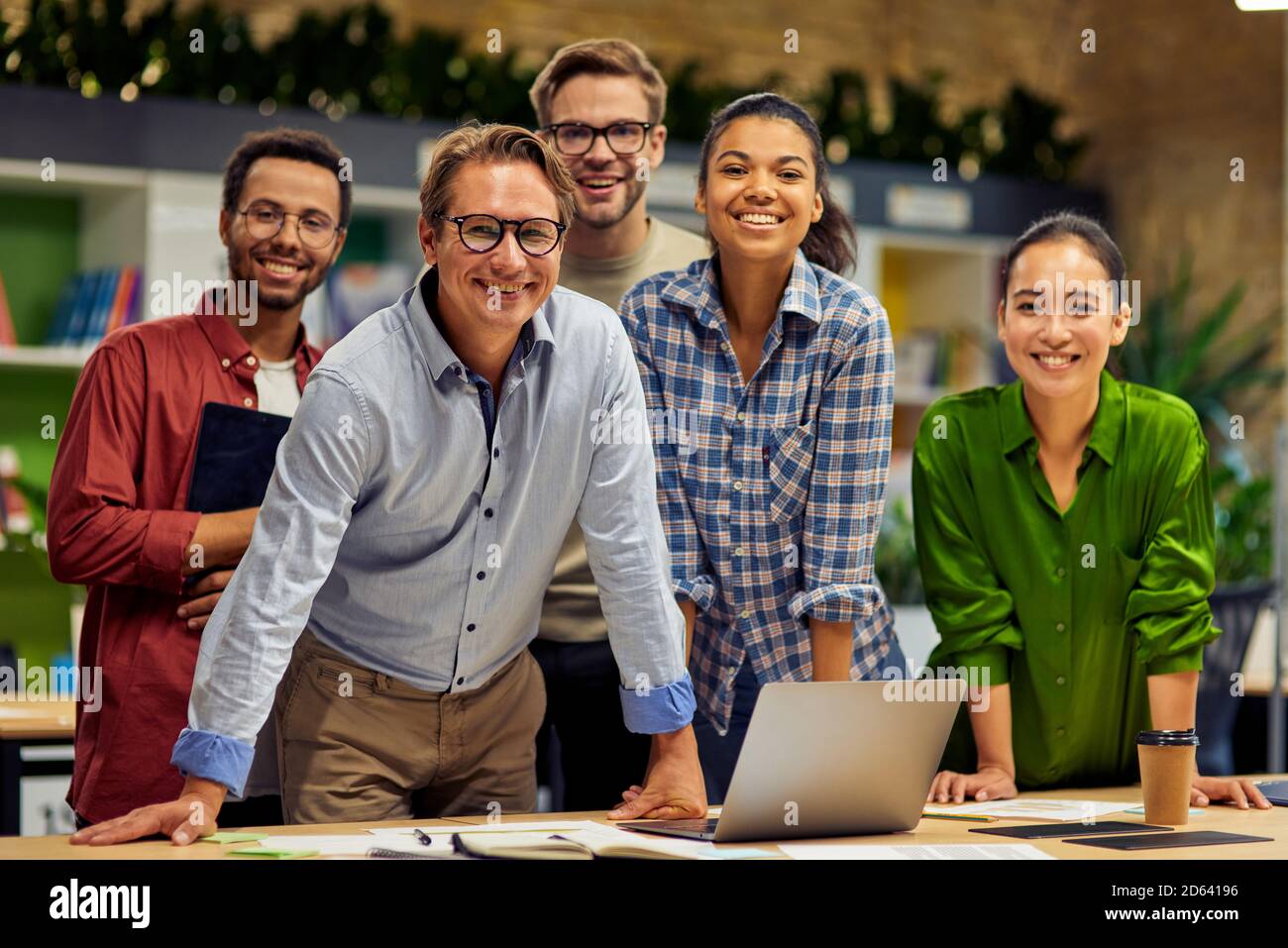 Working as a team. Group of young successful multi ethnic business team looking at camera and smiling while having a meeting in the modern office and coworking space. Business, teamwork, cooperation Stock Photo