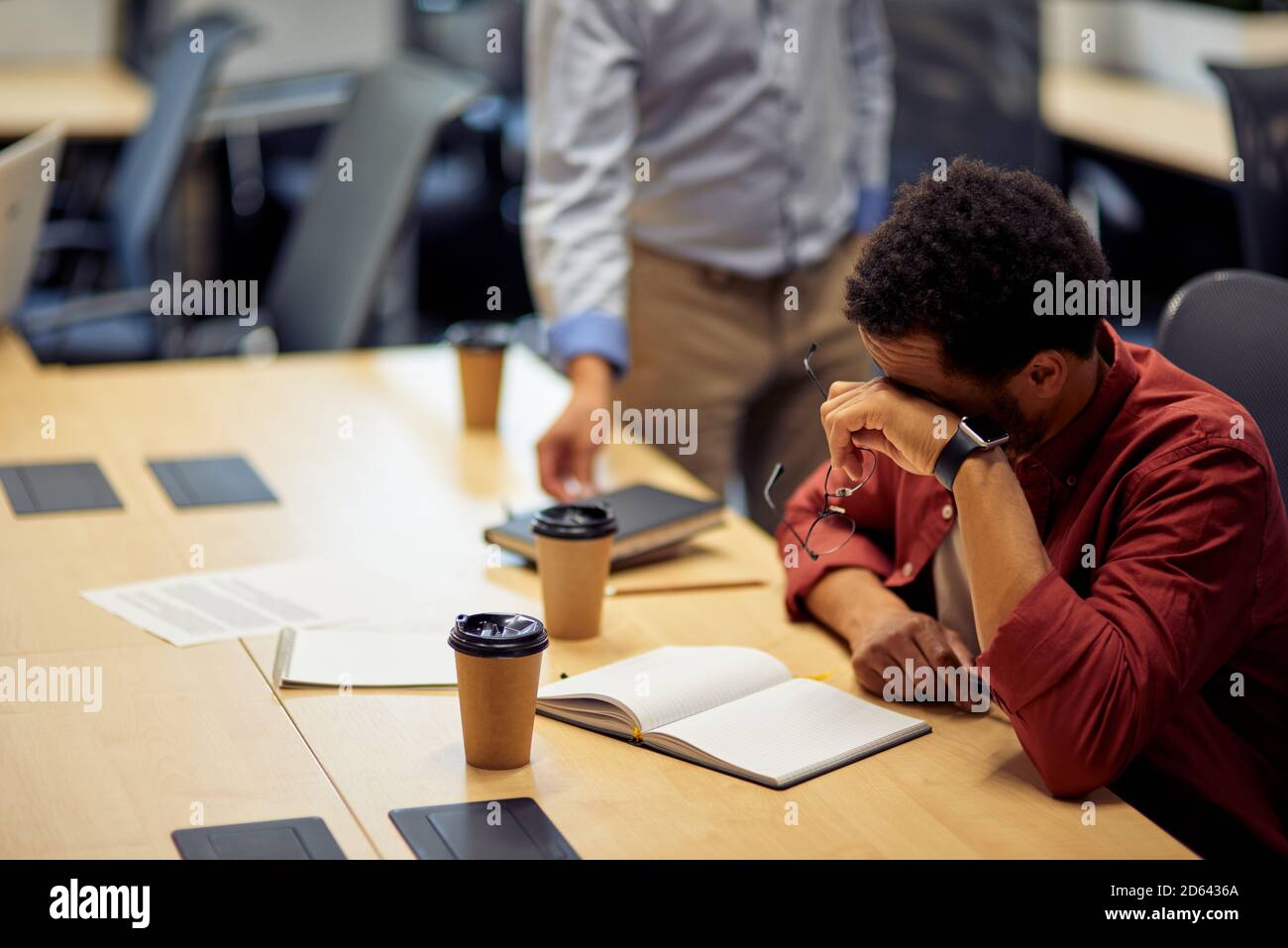 Feeling tired. Young exhausted mixed race man, frustrated male office worker sitting at desk in the modern office. Business problems or stress at work Stock Photo