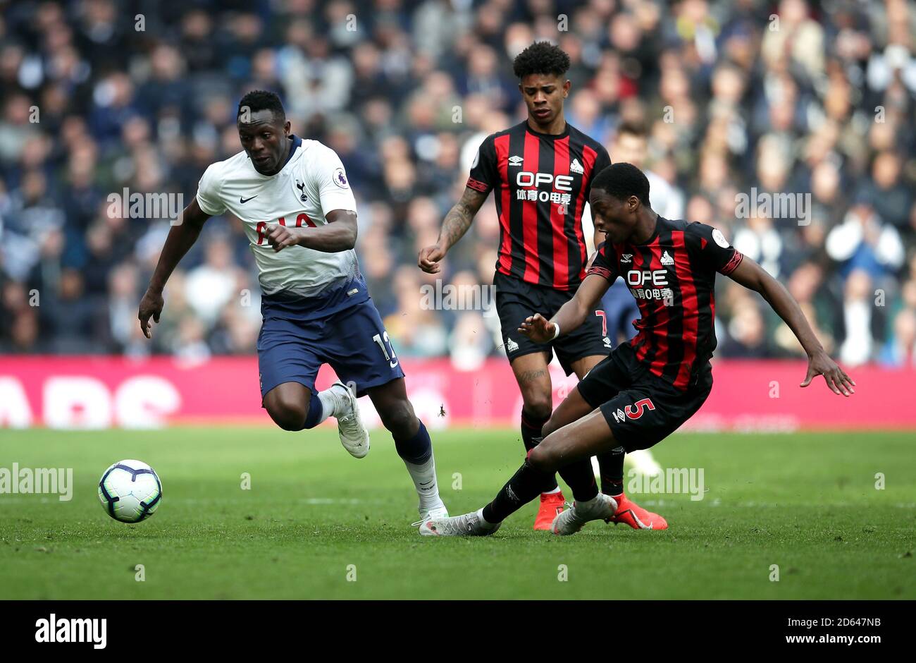 Tottenham Hotspur's Victor Wanyama (left) battles for the ball with Huddersfield Town's Juninho Bacuna and Terence Kongolo (right) Stock Photo