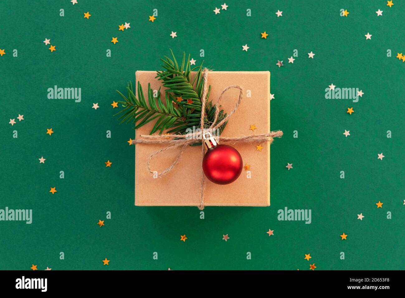 Christmas gift in a box with red ball and confetti on green background. Top view, flat lay. Stock Photo