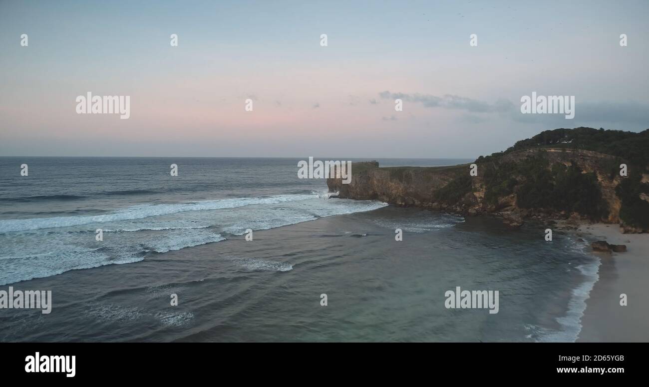 Rock coast at sand beach washed by ocean bay waves aerial view. Nobody tropical Indonesia landscape of cliff shore at sandy seashore. Summer tropic Sumba Island vacation scenery at cinematic morning Stock Photo