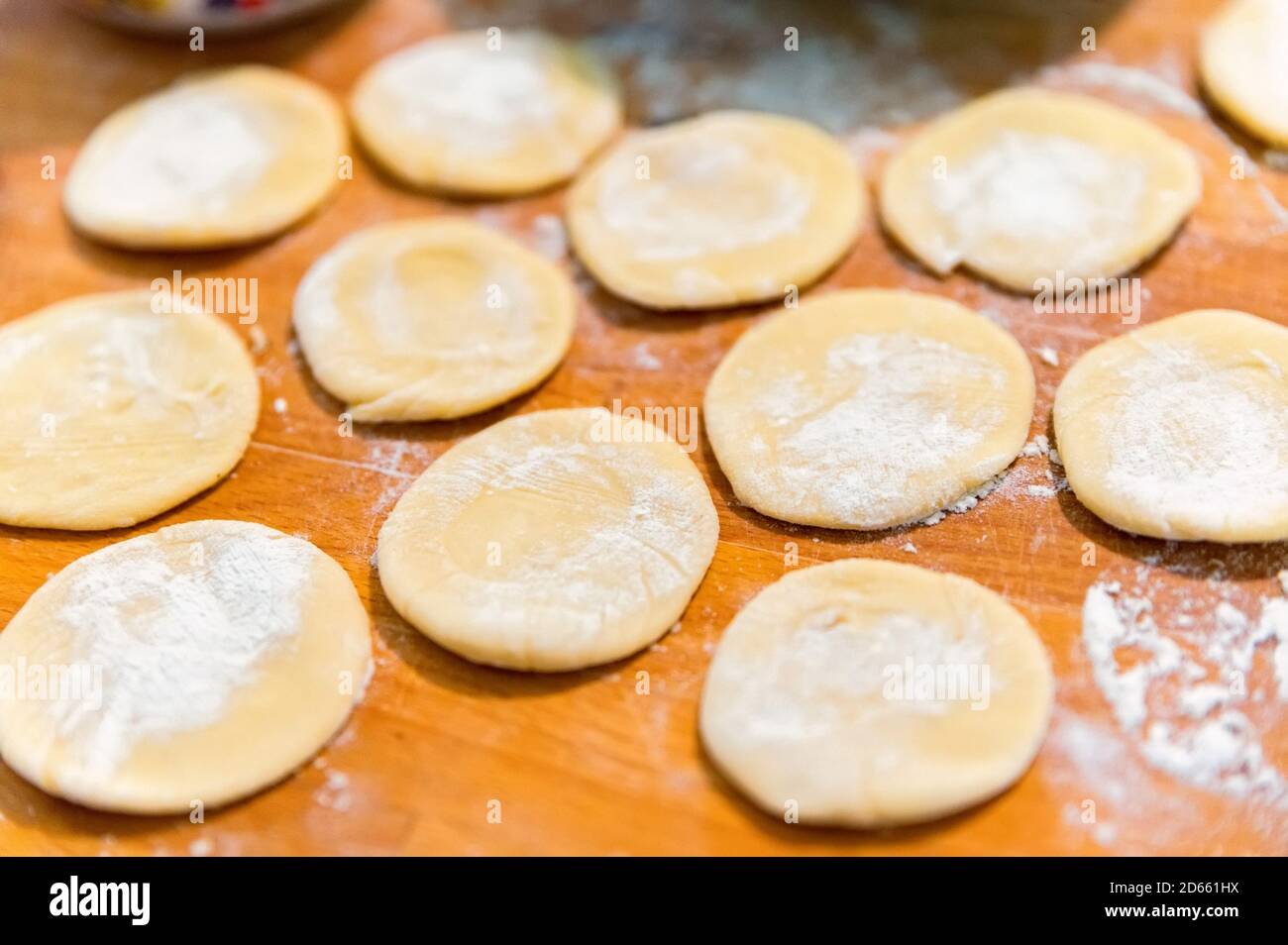 Close-up of small crumpets from raw dough covered with flour on wooden board Stock Photo