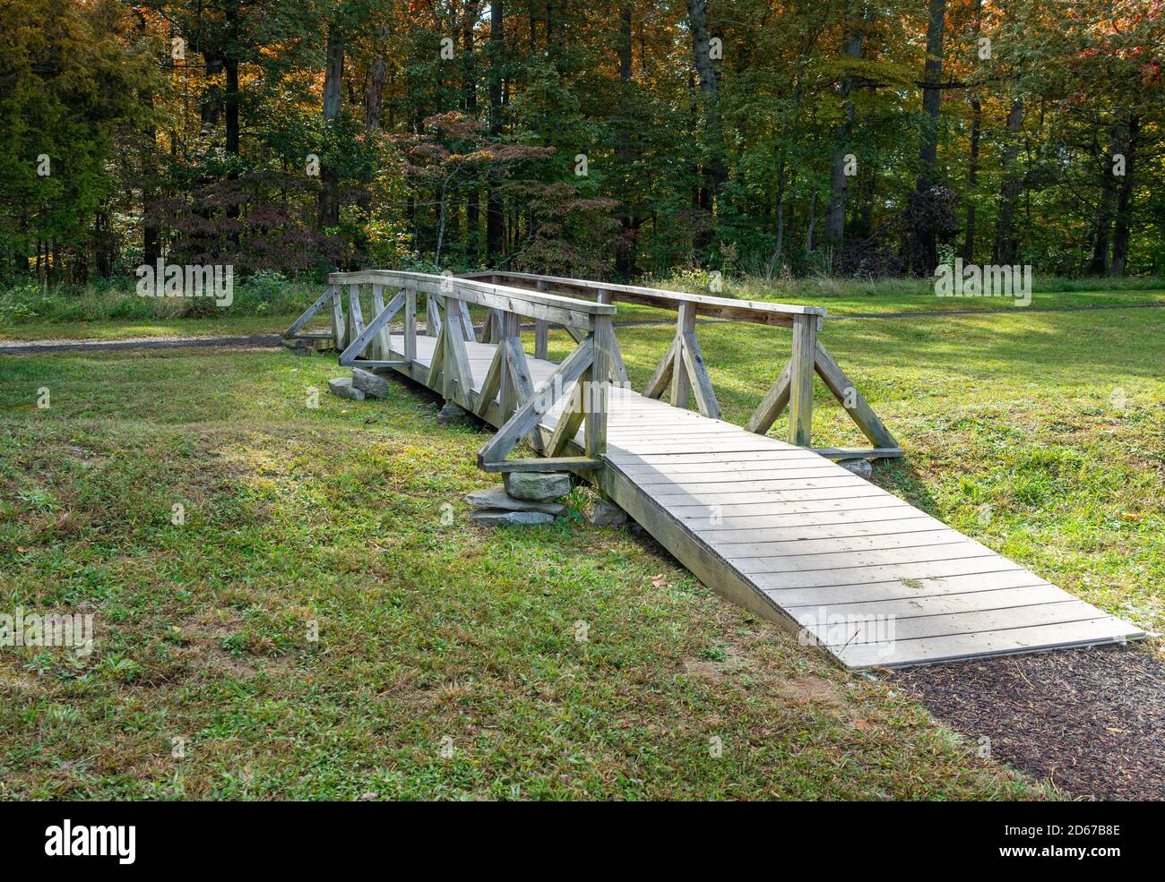 A small wooden footbridge crosses over a small creek in a woodland Stock Photo