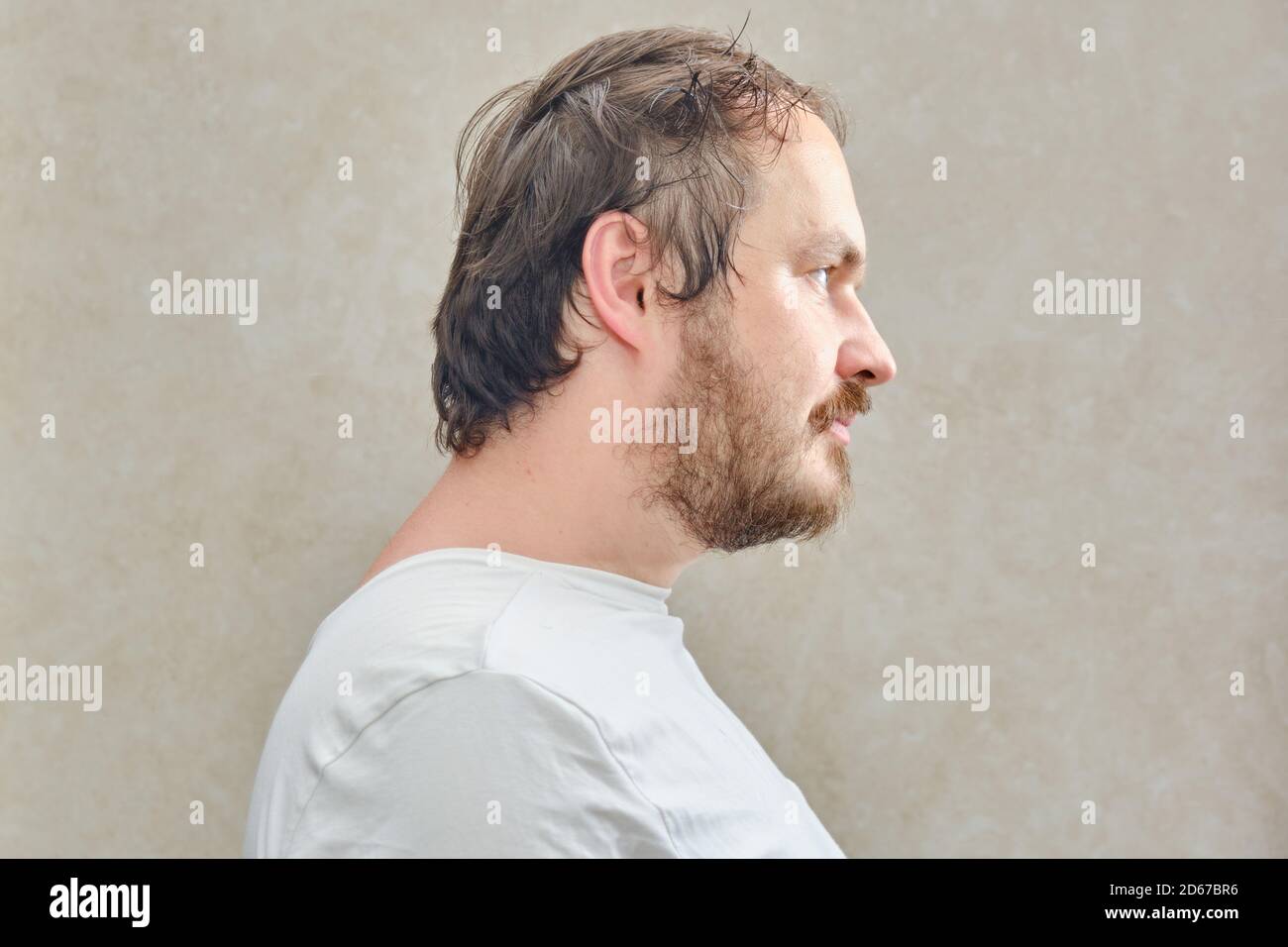 Portrait of a bearded man with a beard in a white t-shirt, close-up. Face of a man with a beard 35-40 years old on a beige background Stock Photo
