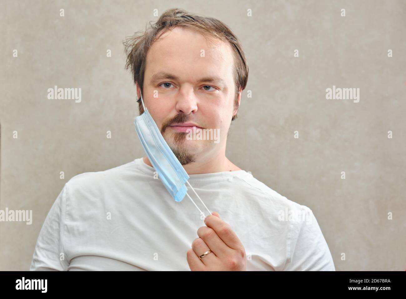 The man removes the medical mask under which the half-shaved beard and disheveled hair. The concept of closed salons and barbershop during the isolati Stock Photo