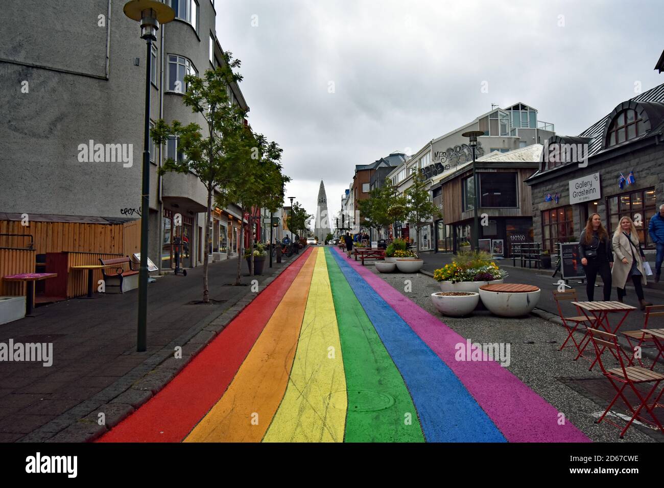 The bright colours of a rainbow painted road (Skolavordustigur) contrasts with the grey skies, leads to Hallgrimskirkja Church in Reykjavik, Iceland. Stock Photo