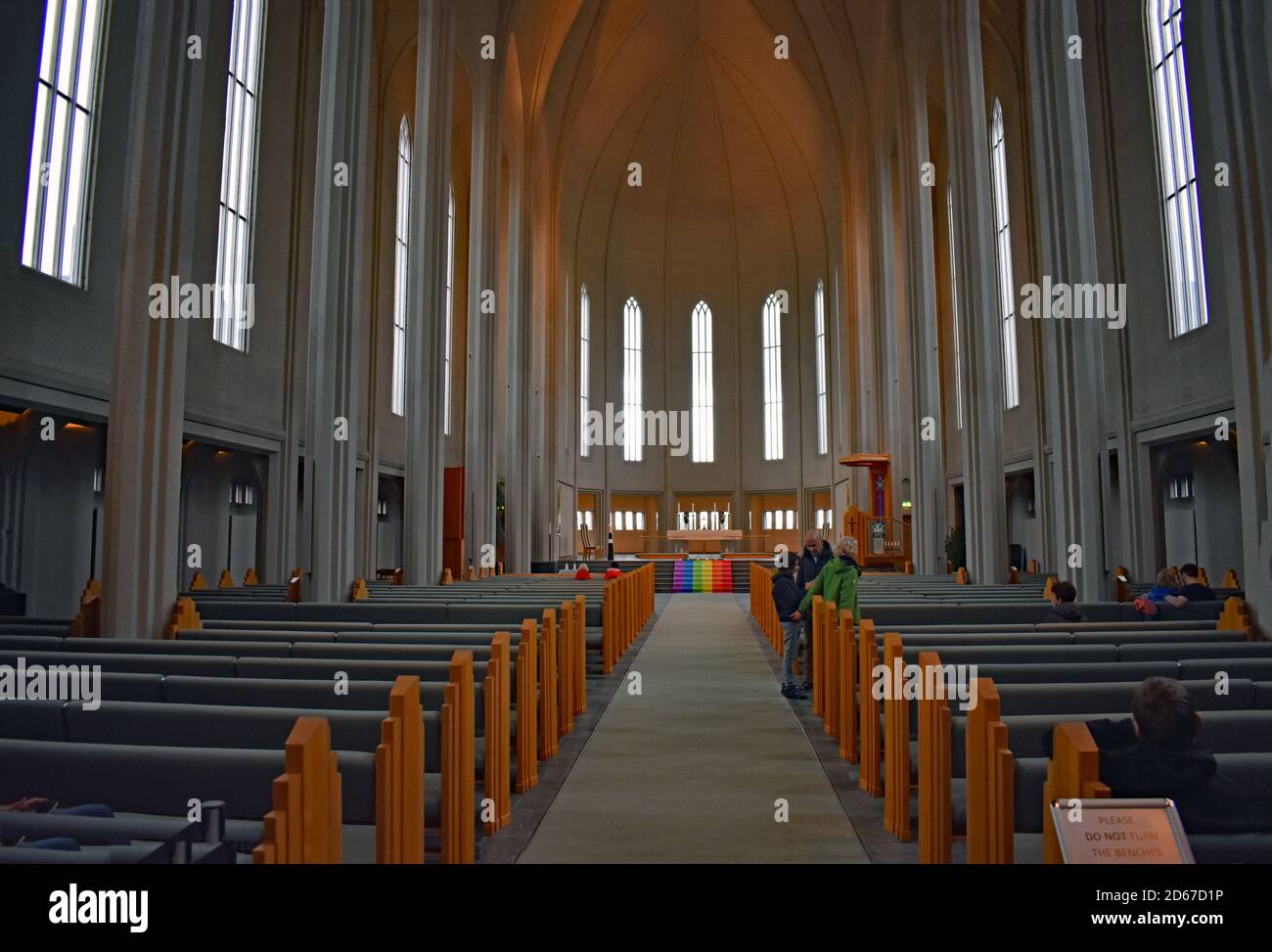 The interior of Hallgrimskirkja Church in Reykjavik. Iceland.  The alter can be seen displaying a rainbow flag (gay pride) and visitors gather inside. Stock Photo