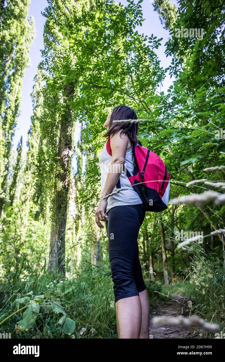 Vertical low angle shot of a female hiker with a backpack surrounded by a lush greenery Stock Photo