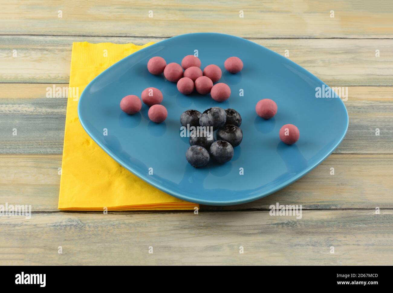 Blueberries dipped in ruby cacao chocolate and fresh raw blueberries on blue snack plate with yellow napkin Stock Photo
